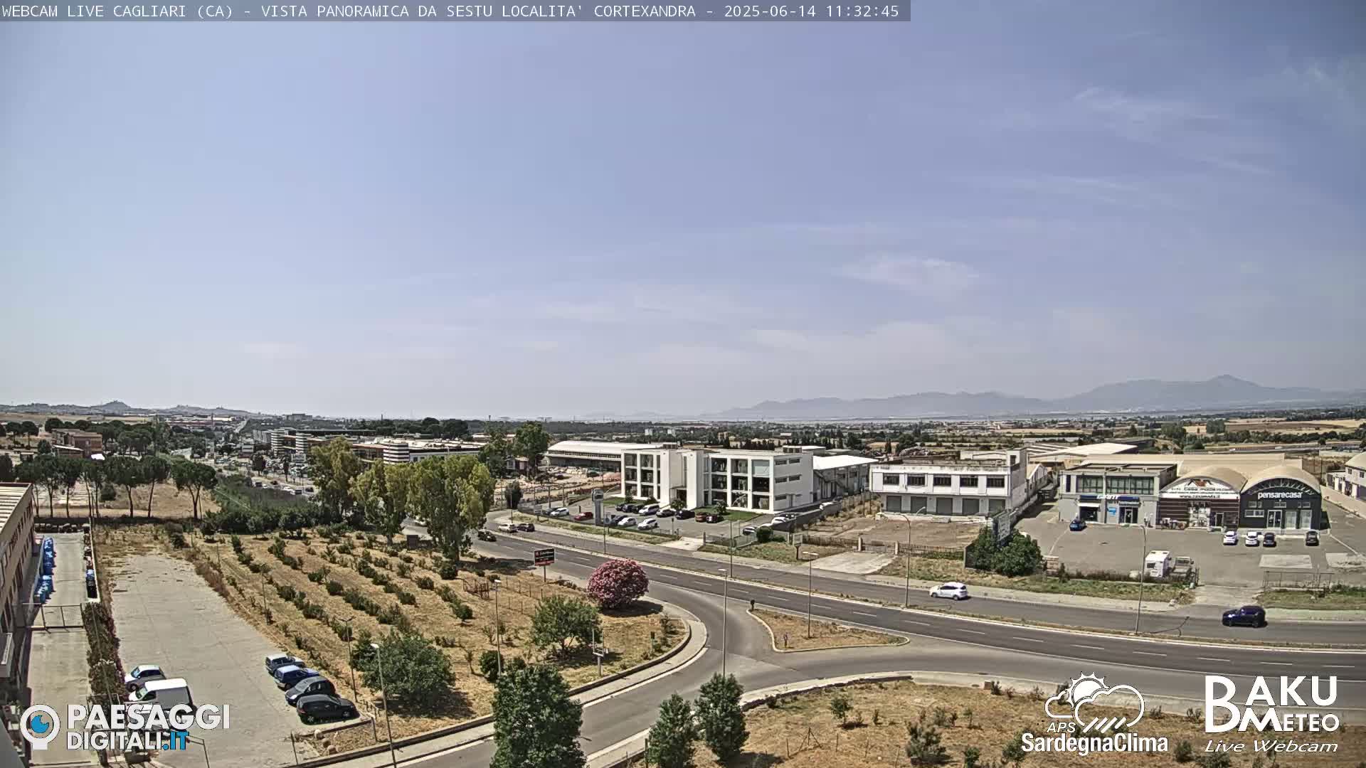 A sunny day reveals a wide shot of a suburban area with roads, buildings, and sparse vegetation, mountains visible in the distance.