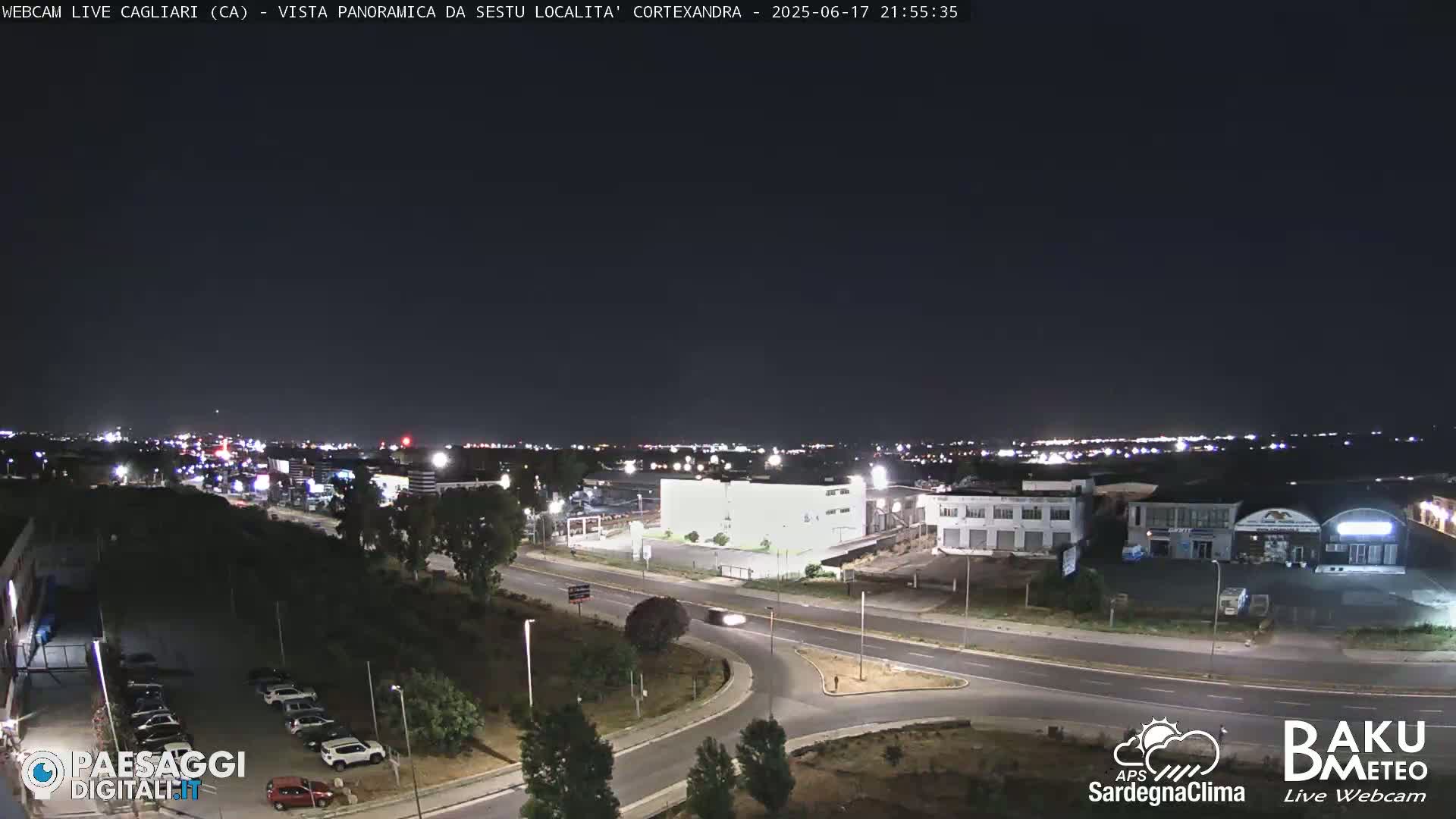 A nighttime, clear-sky view of a highway intersection and surrounding buildings and parking lots, illuminated by streetlights and distant city lights.