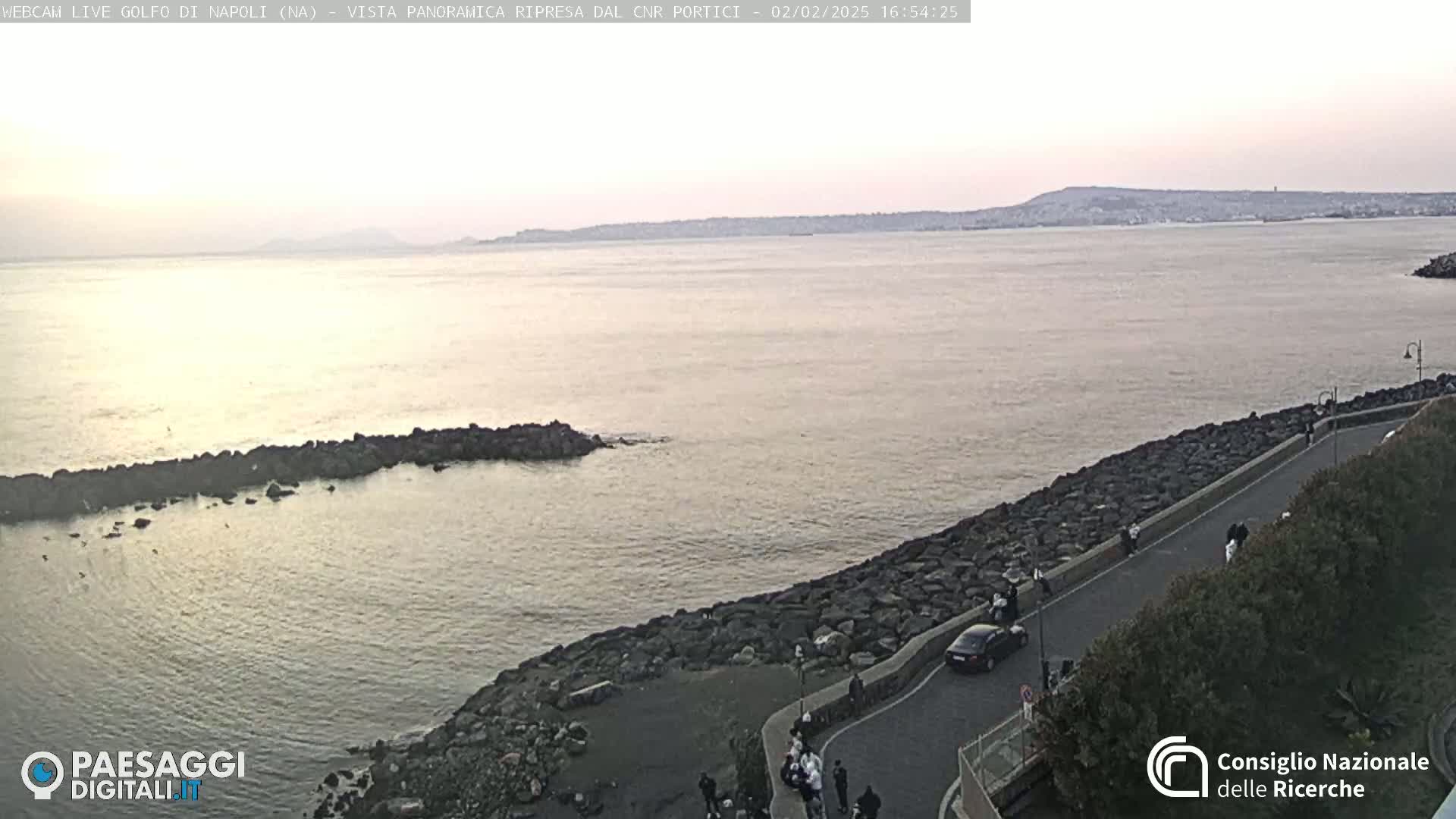 A rocky shoreline curves gently around a calm body of water under a dusky sky, with a distant landmass visible on the horizon.