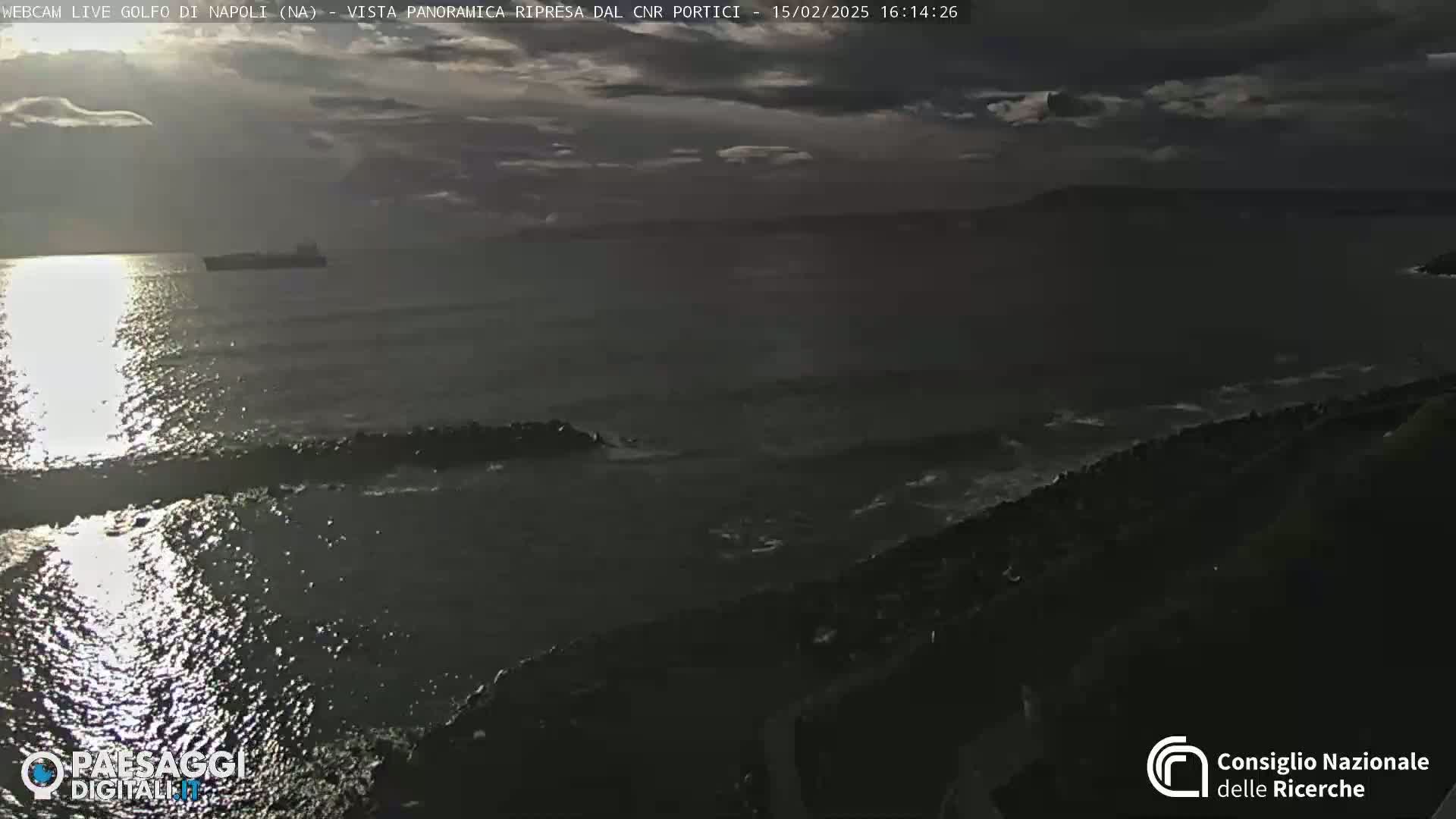 A dark, overcast day shows a somewhat choppy sea with a distant ship and rocky shoreline.