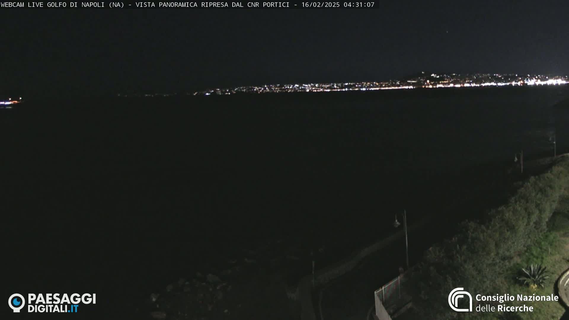 A nighttime, long-range view shows a dark body of water with a distant city skyline illuminated by lights.