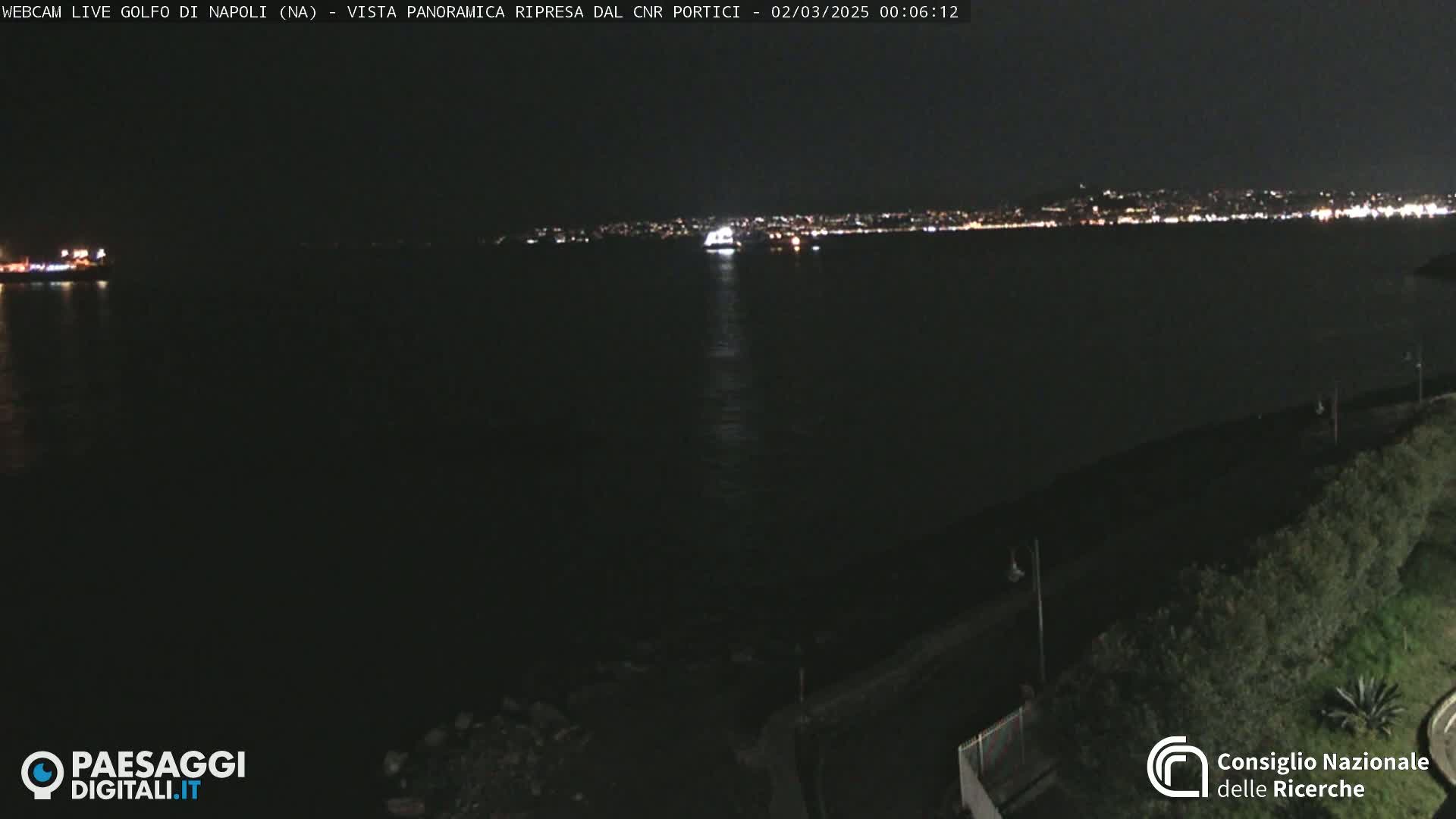 A nighttime, panoramic view of a dark body of water with a distant city skyline illuminated by lights.