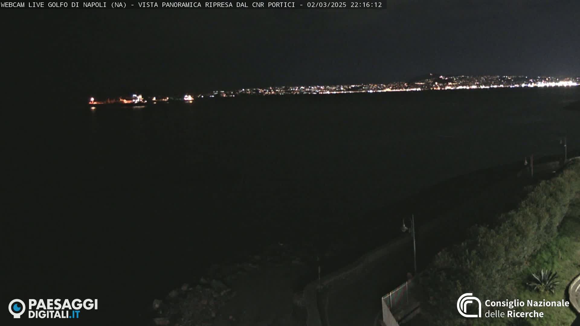 A nighttime, long shot of a dark body of water with a city skyline faintly illuminated in the distance.