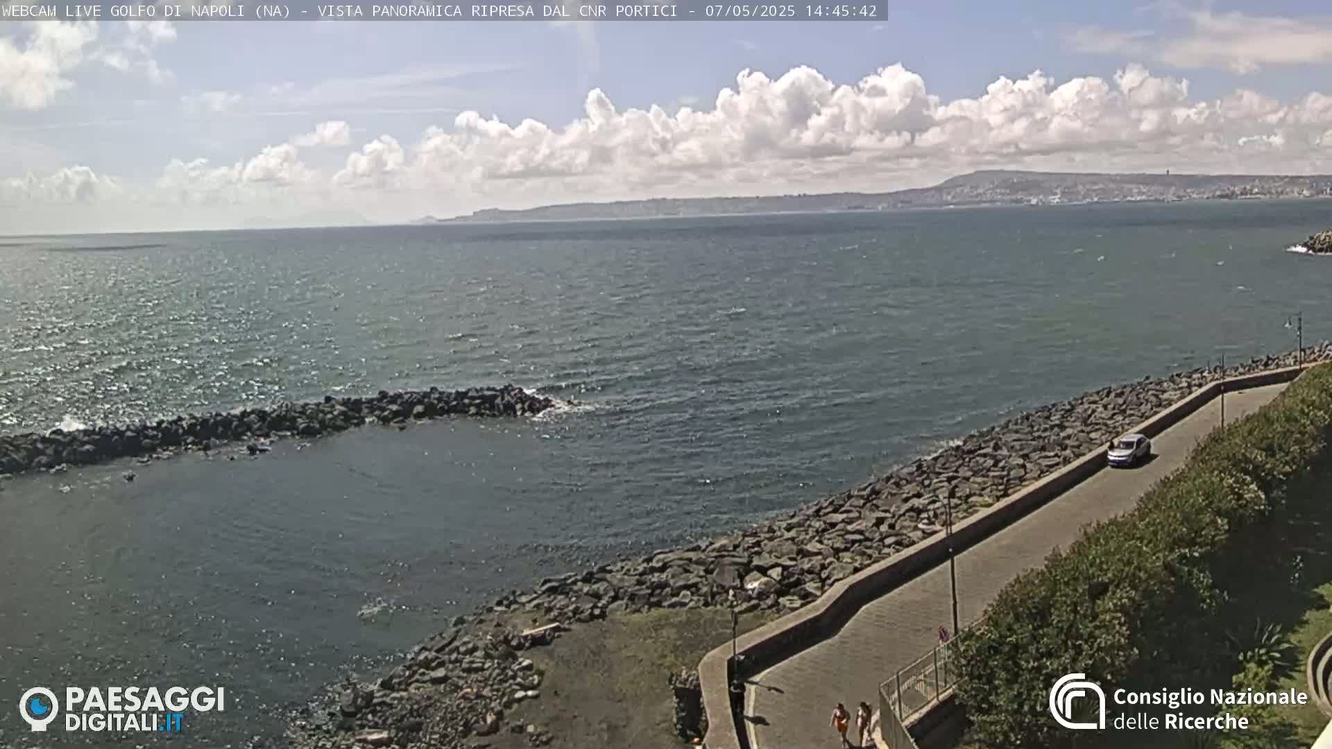 A partly cloudy day reveals a seaside view of a rocky shoreline, a calm sea, and a distant landmass under a partly cloudy sky.