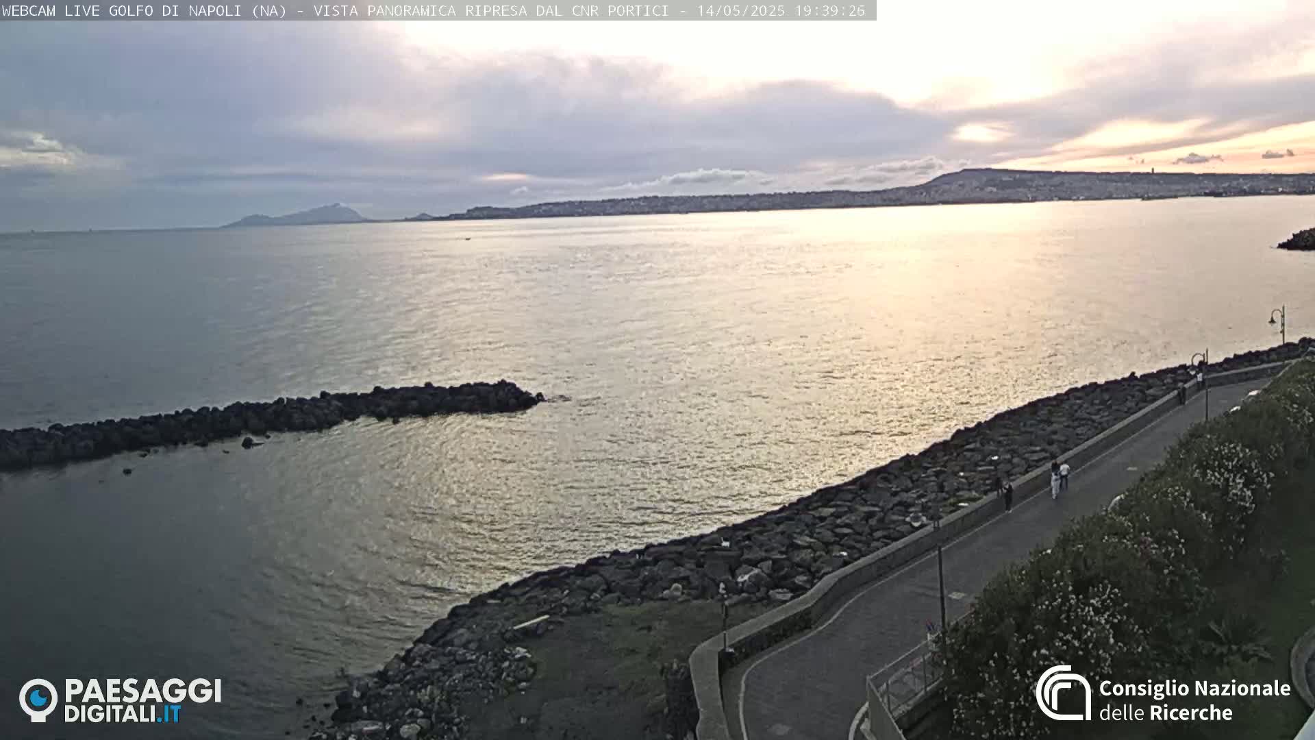 A calm sea under a partly cloudy sunset sky stretches to a distant coastline.