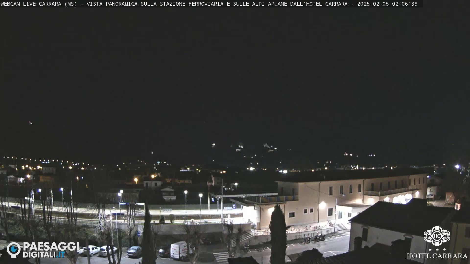 A nighttime, long shot of a town, including a train station and a hotel, under a clear, dark sky.