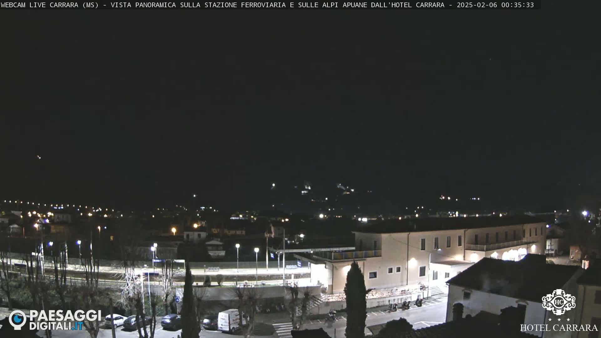 A nighttime, panoramic view of a town's railway station and surrounding buildings under a clear, dark sky.