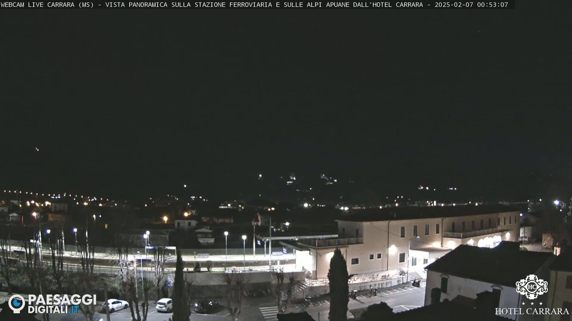 A nighttime view of a town with a train station and a large building, under a clear, dark sky.
