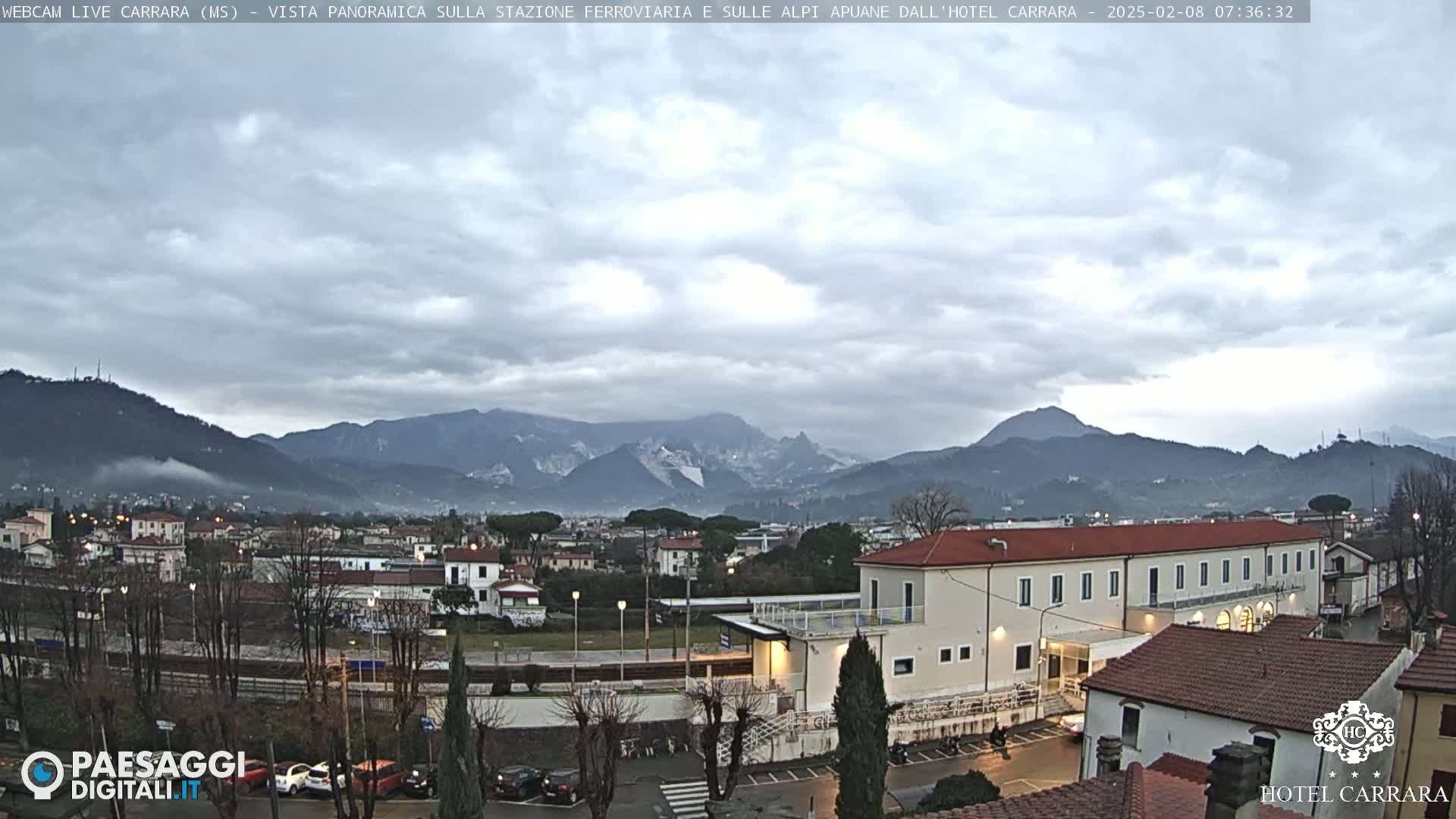 A panoramic view of a town nestled in a valley, with mountains in the background under a cloudy sky.