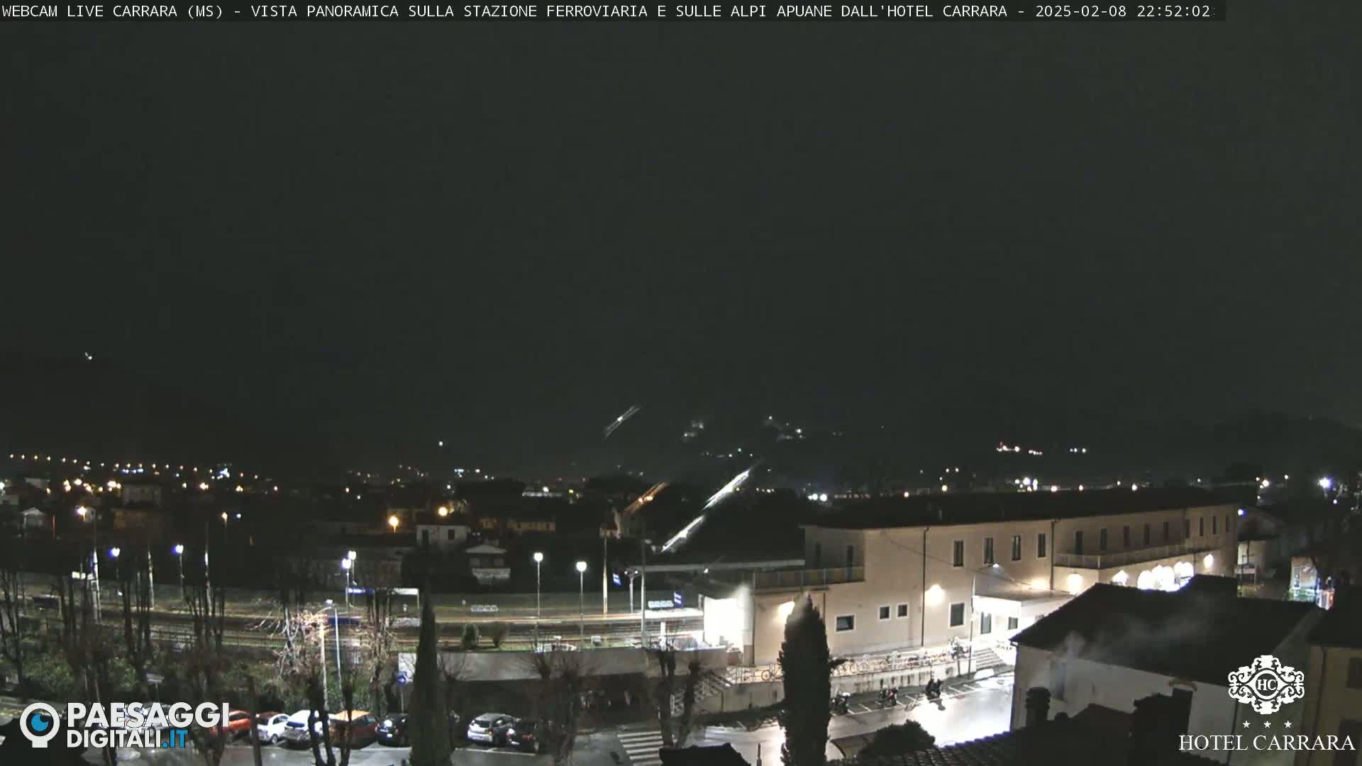 A nighttime, panoramic view of a town with a train station and buildings under a dark sky.