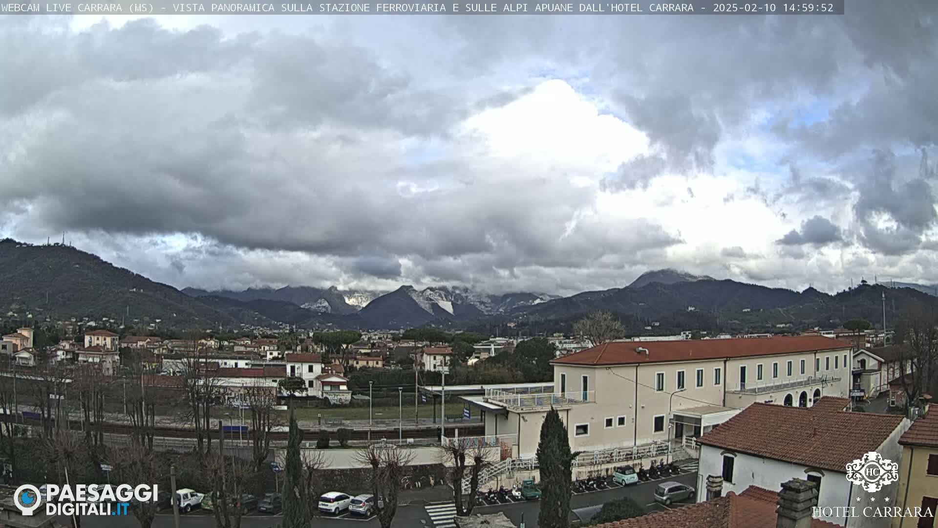 A panoramic view of a town nestled in a valley, with overcast skies and snow-capped mountains in the distance.