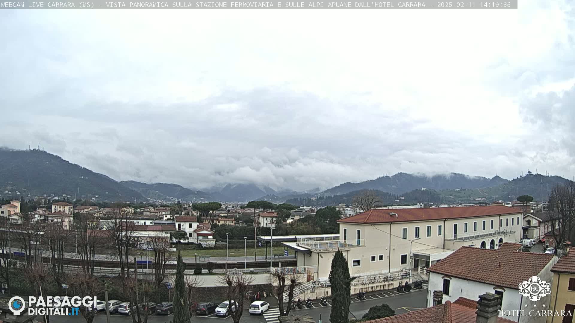 A cloudy day overlooks a town nestled in a valley between low, tree-covered mountains.