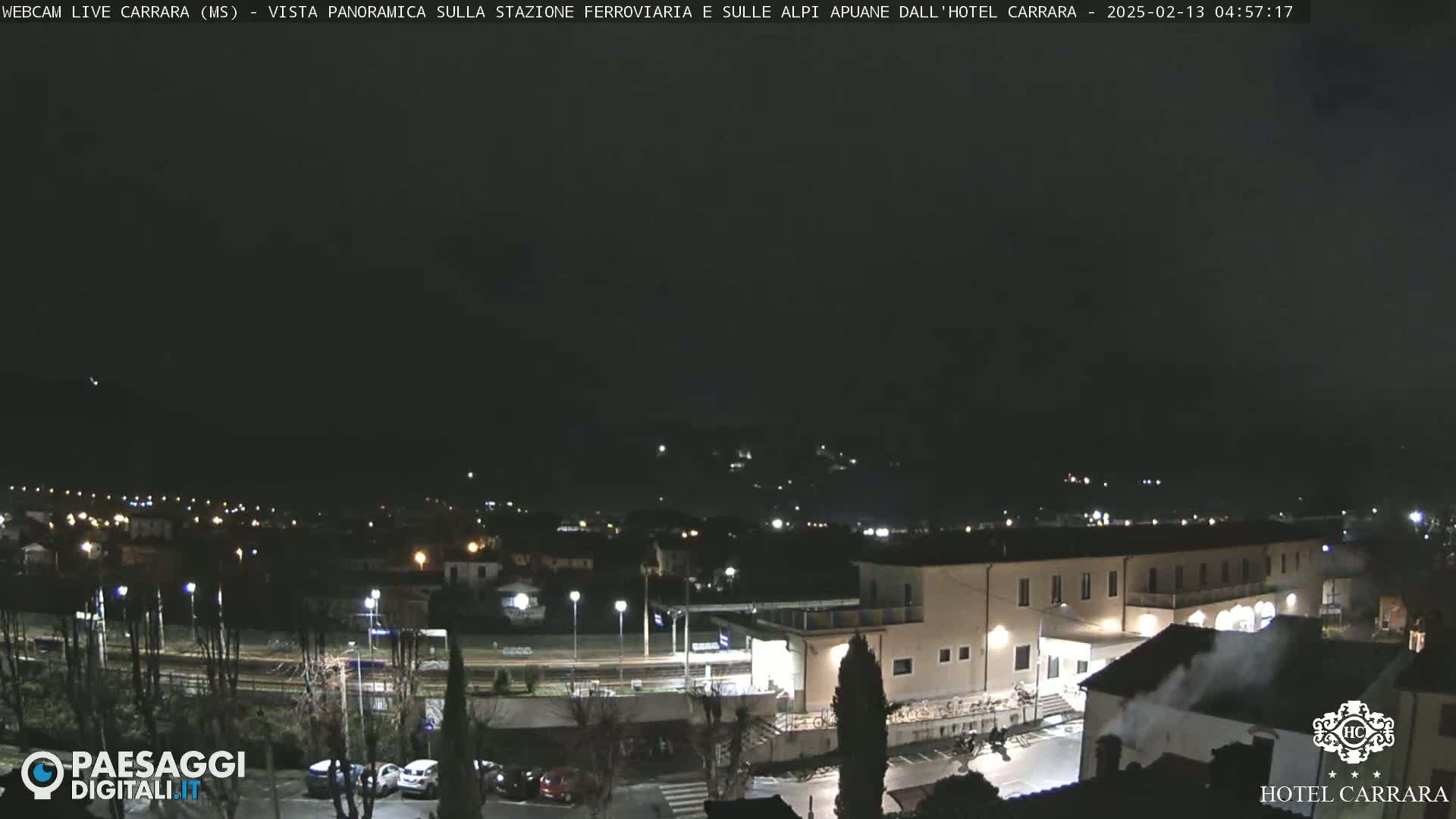 A nighttime, panoramic view of a town with a train station and a large building, possibly a hotel, under a dark, clear sky.