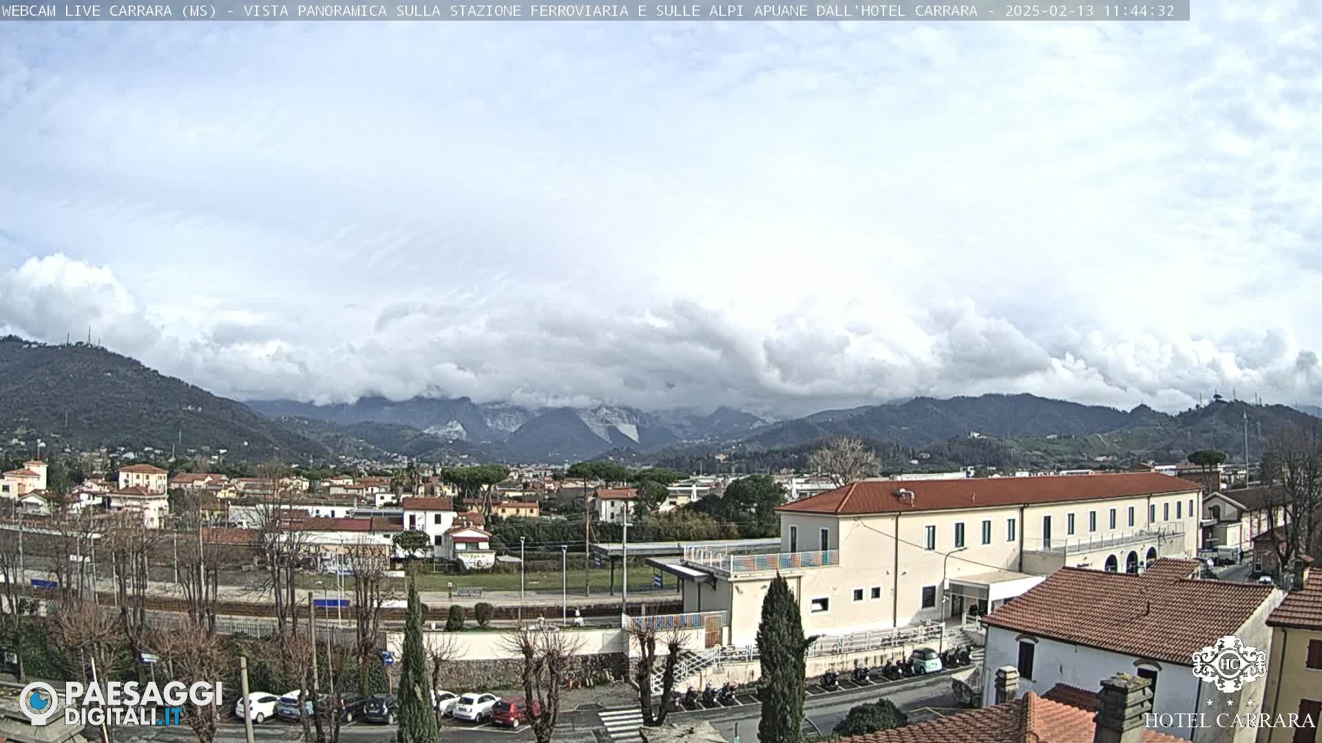 A cloudy day reveals a panoramic view of a town nestled in a valley, mountains rising in the background.