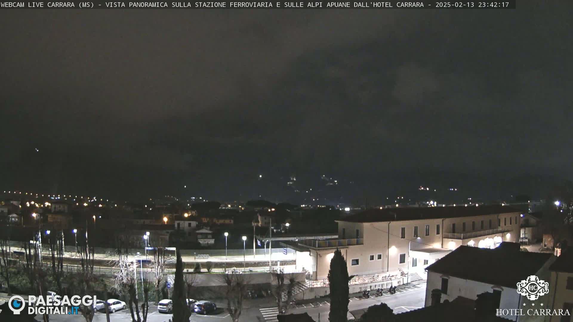 A nighttime view of a town with a train station and a hotel, under a dark, cloudy sky.