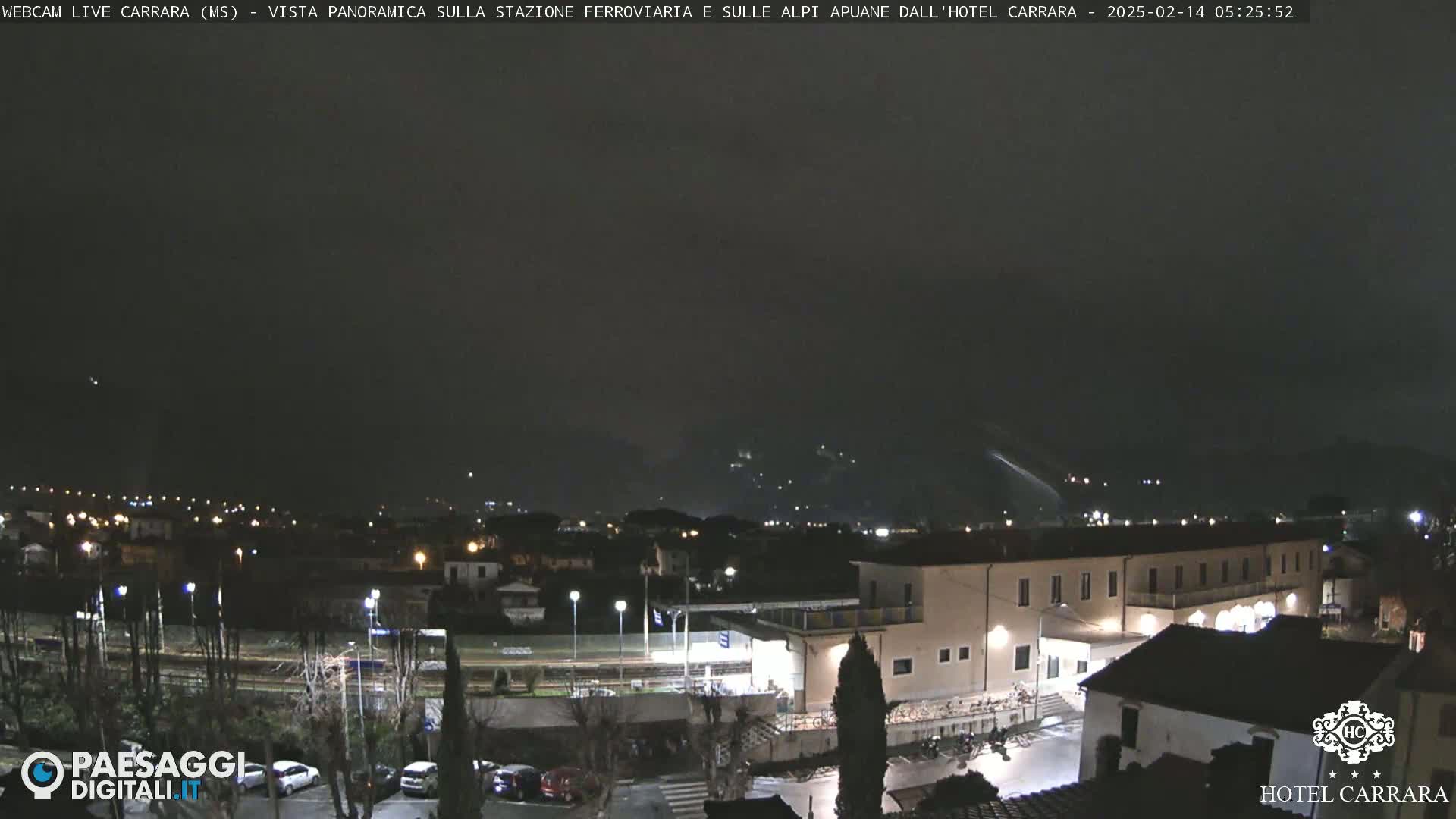 A nighttime view of a town with a train station and buildings under a dark, possibly overcast sky.
