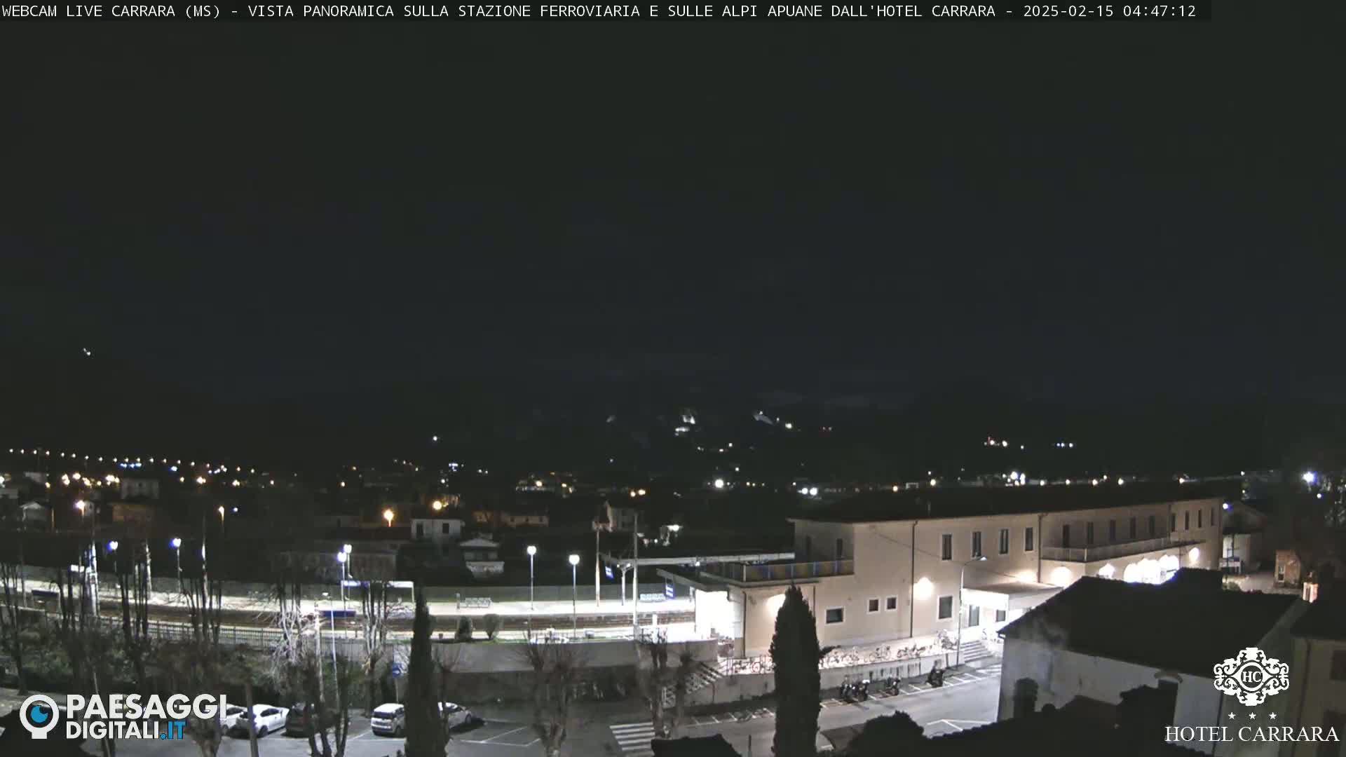 A nighttime, panoramic view of a town with a train station and a hotel, under a dark sky.