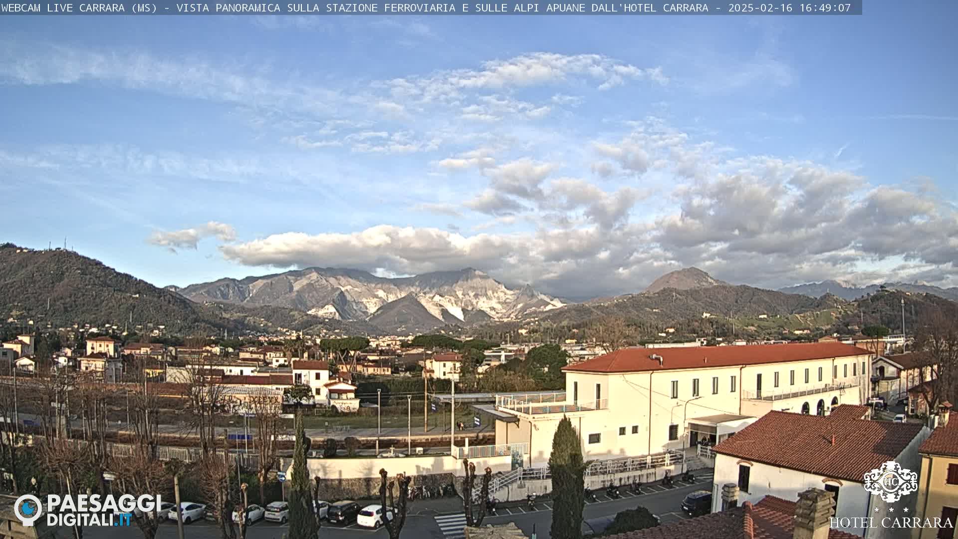 A partly cloudy day reveals a panoramic view of a town nestled in a valley, with mountains in the background.