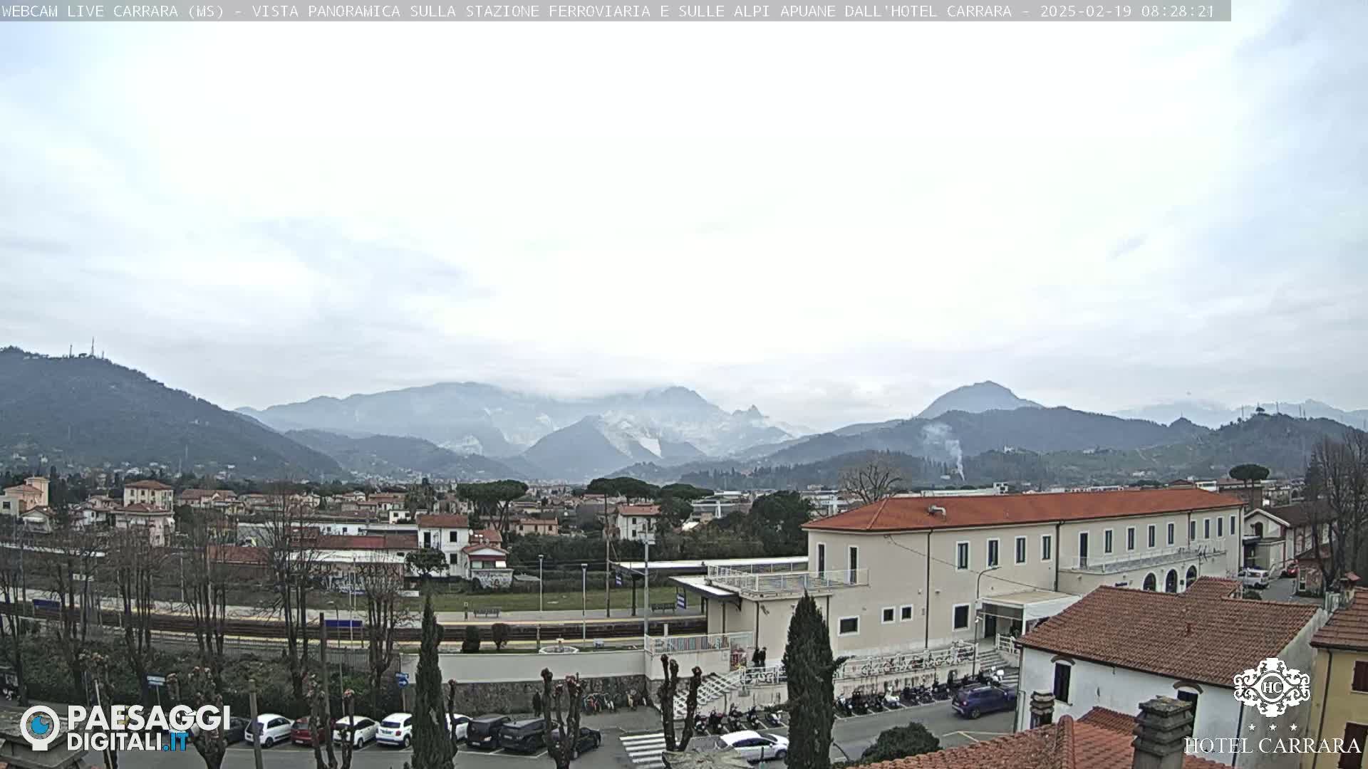 A long shot of a town nestled in a valley, with mountains in the background under an overcast sky.