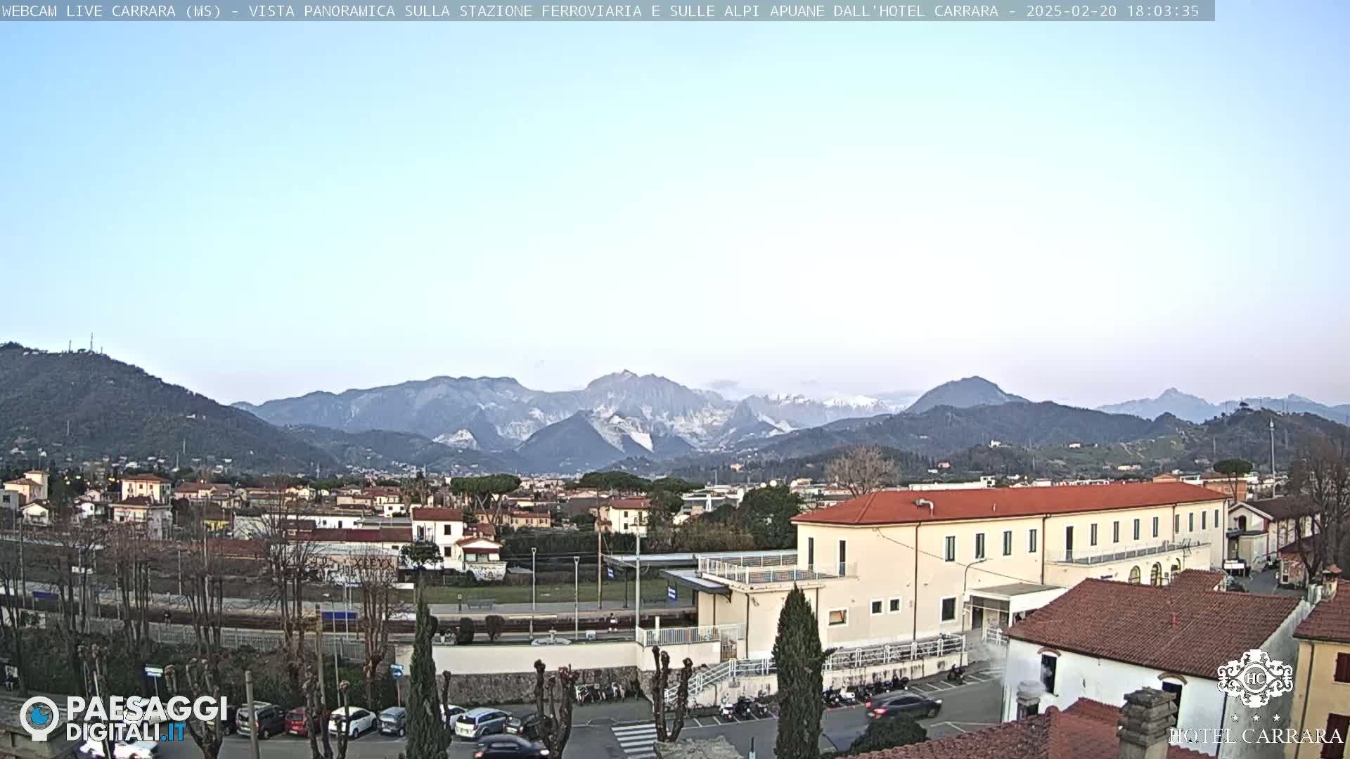 A panoramic view of a town nestled in a valley, with mountains in the background under a clear, light-blue sky.