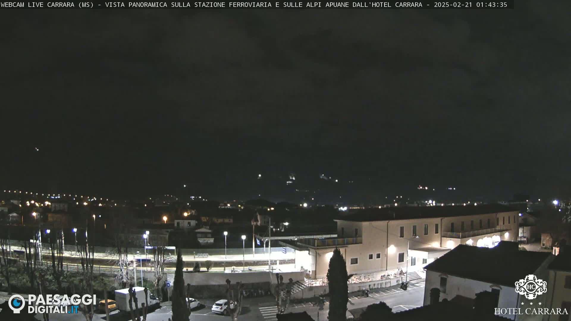 A nighttime, panoramic view of a town with a train station and buildings, under a dark sky.