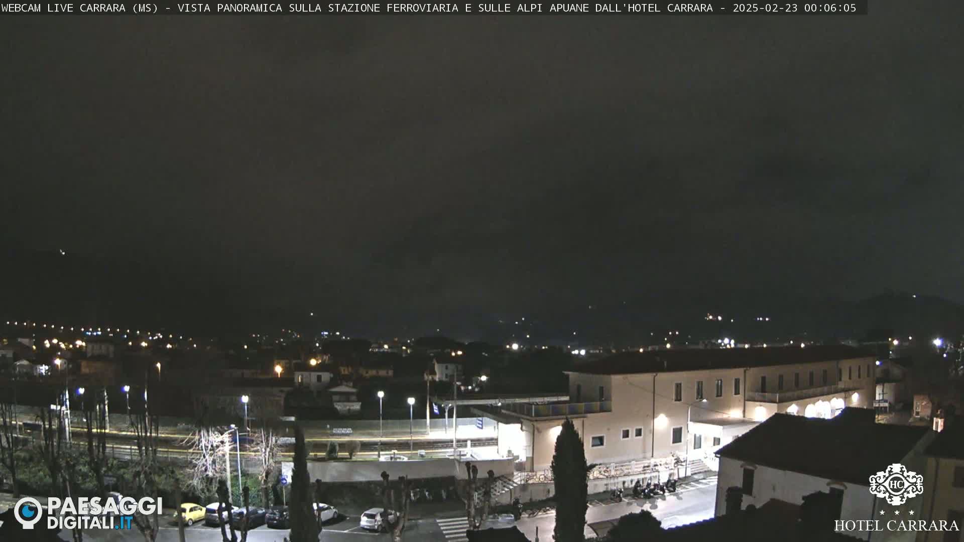 A nighttime, panoramic view of a town with a train station and buildings, under a dark, overcast sky.
