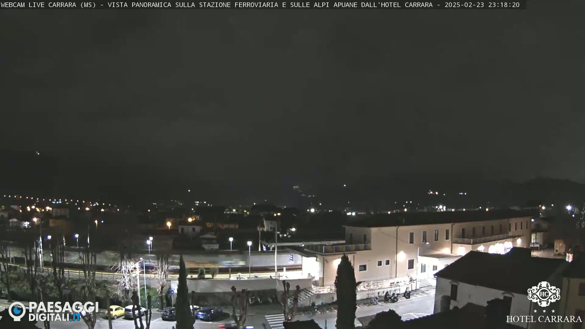 A nighttime, panoramic view of a town with a train station and a hotel, under a dark, mostly clear sky.