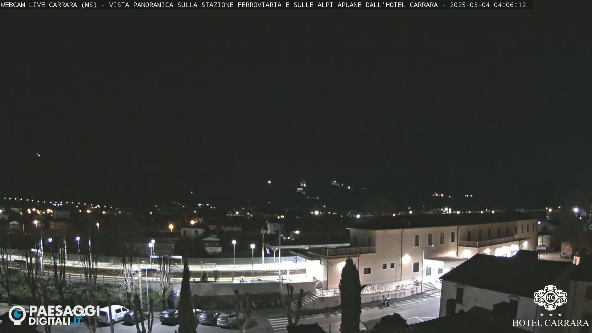 A nighttime, panoramic view of a town with a train station and a hotel, under a clear, dark sky.
