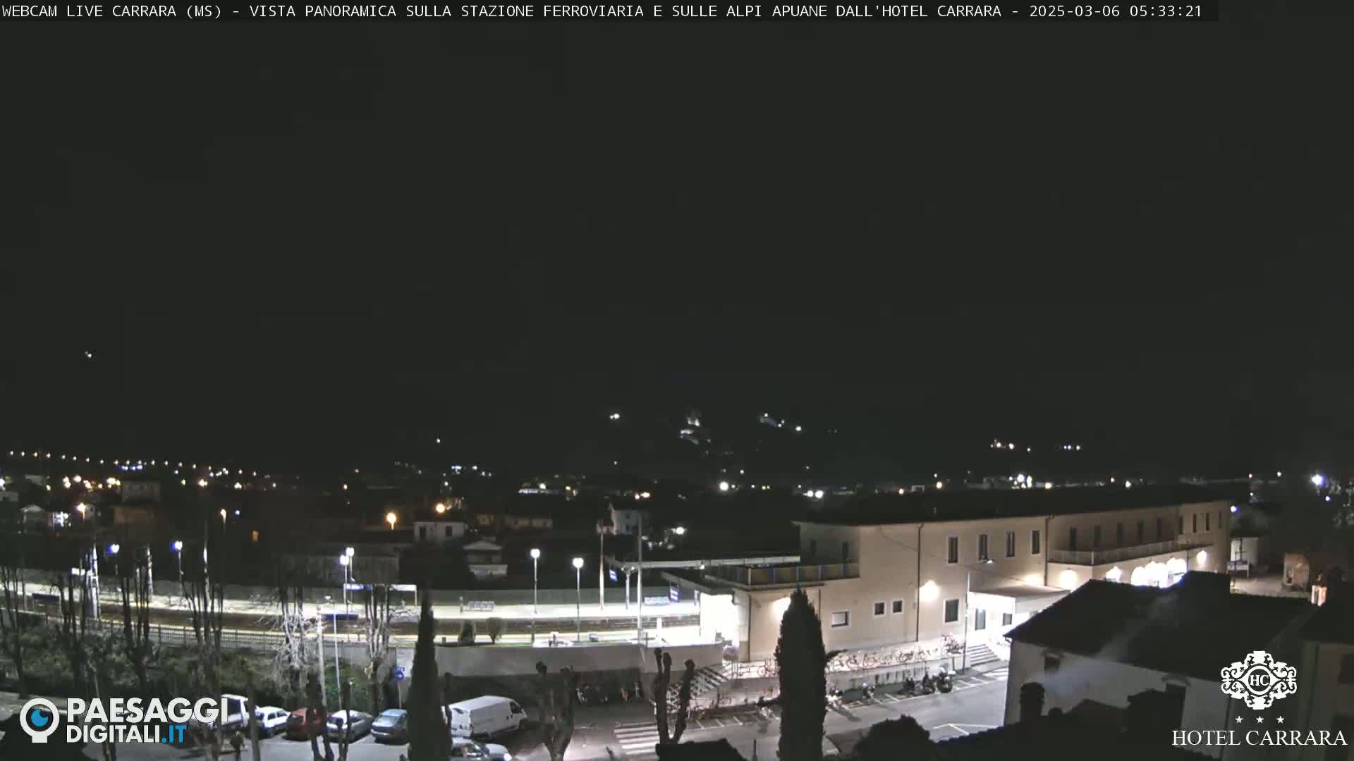 A nighttime, panoramic view of a town with a train station and hotel, under a clear, dark sky.