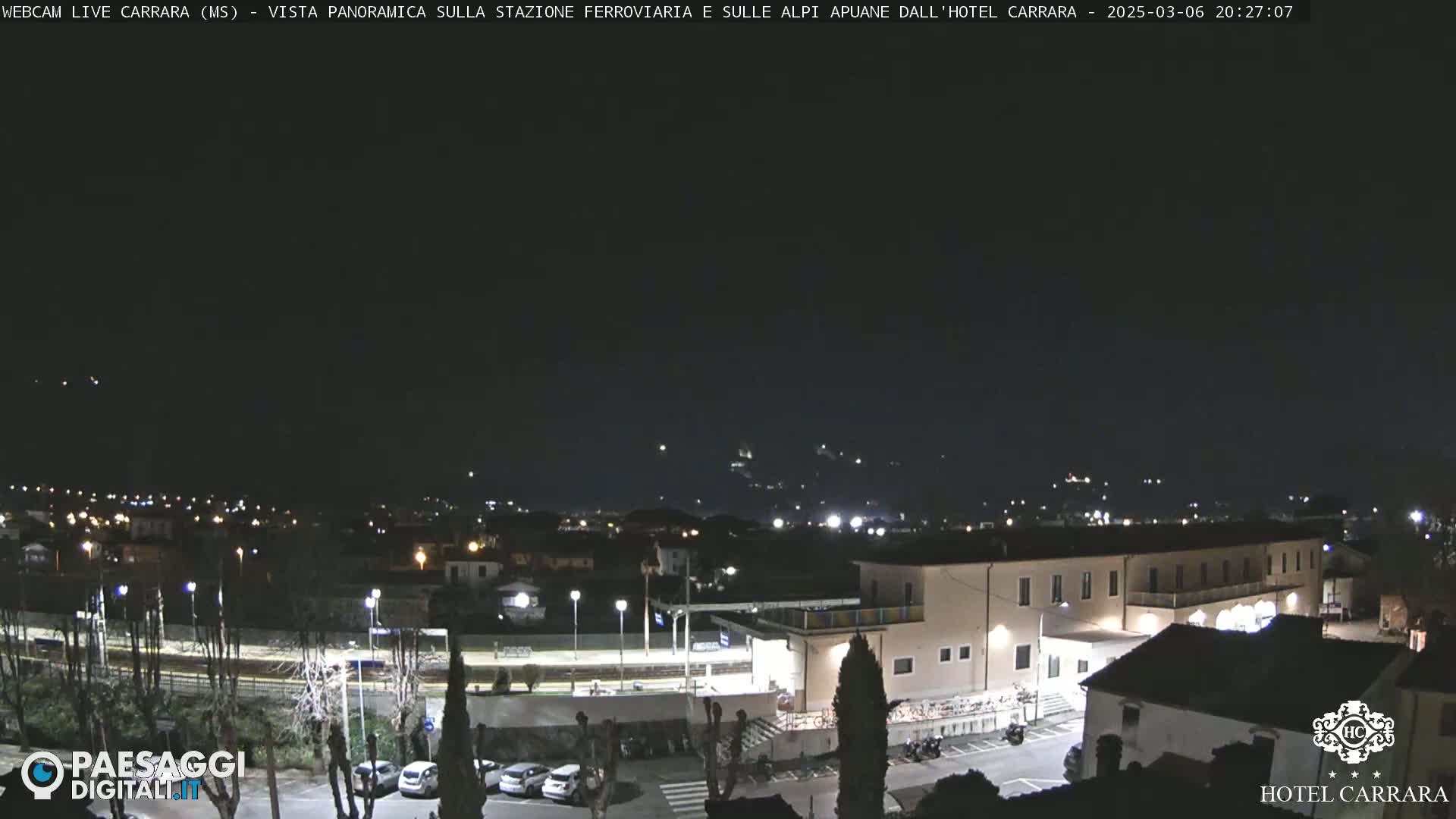 A nighttime panoramic view of a town with a train station and a hotel, under a clear, dark sky.