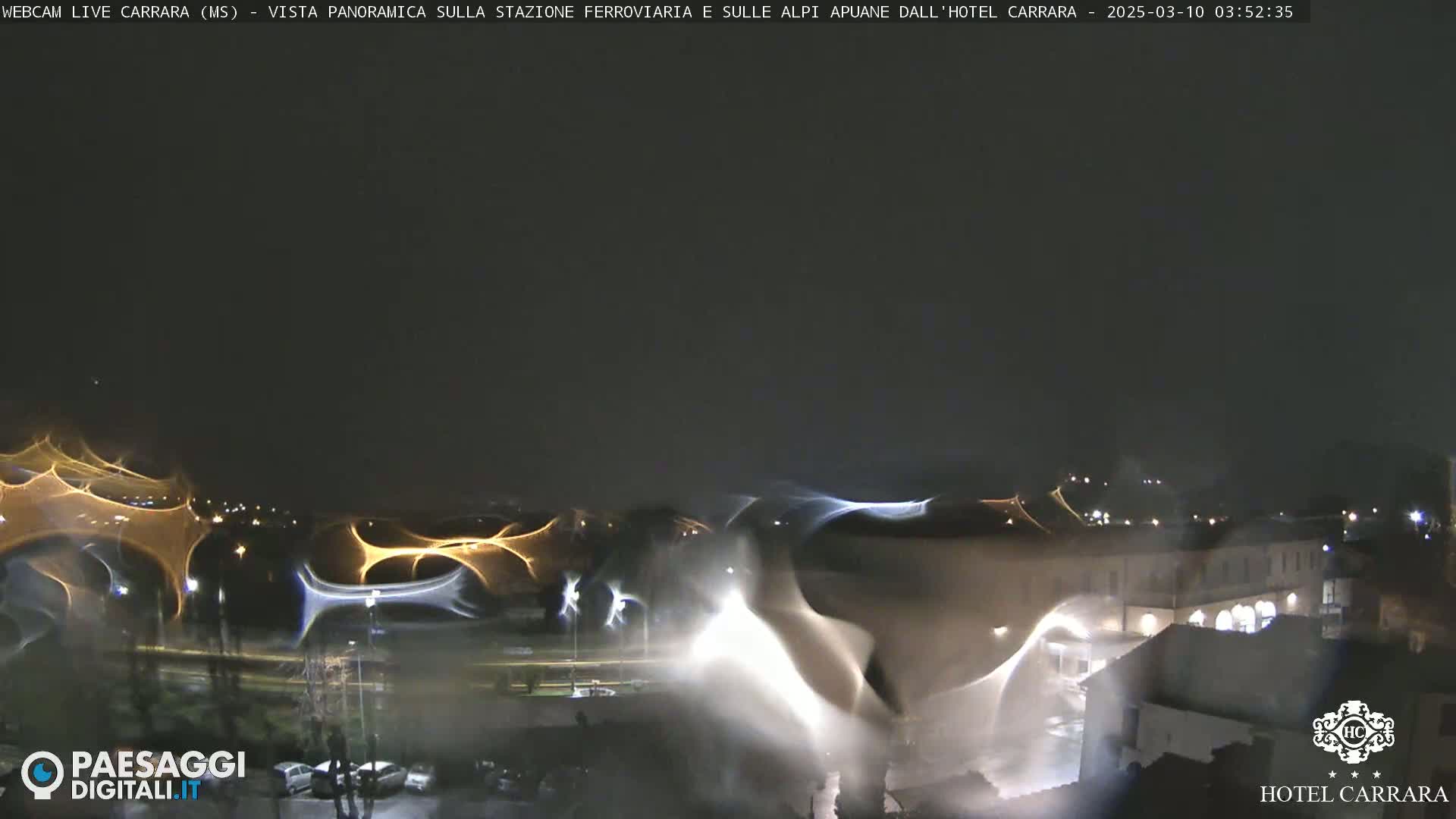 A nighttime view of city lights and buildings, distorted by what appears to be rain or condensation on a window.