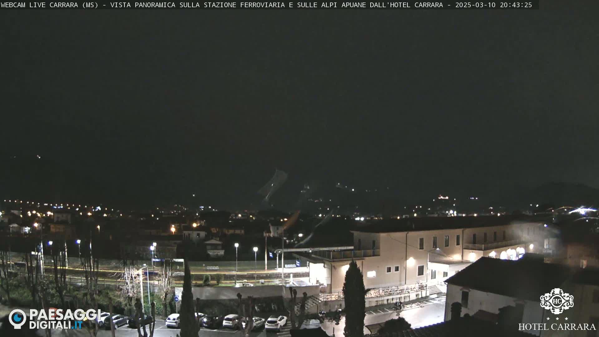 A nighttime, panoramic view of a town with a train station and a hotel, under a dark, mostly clear sky.