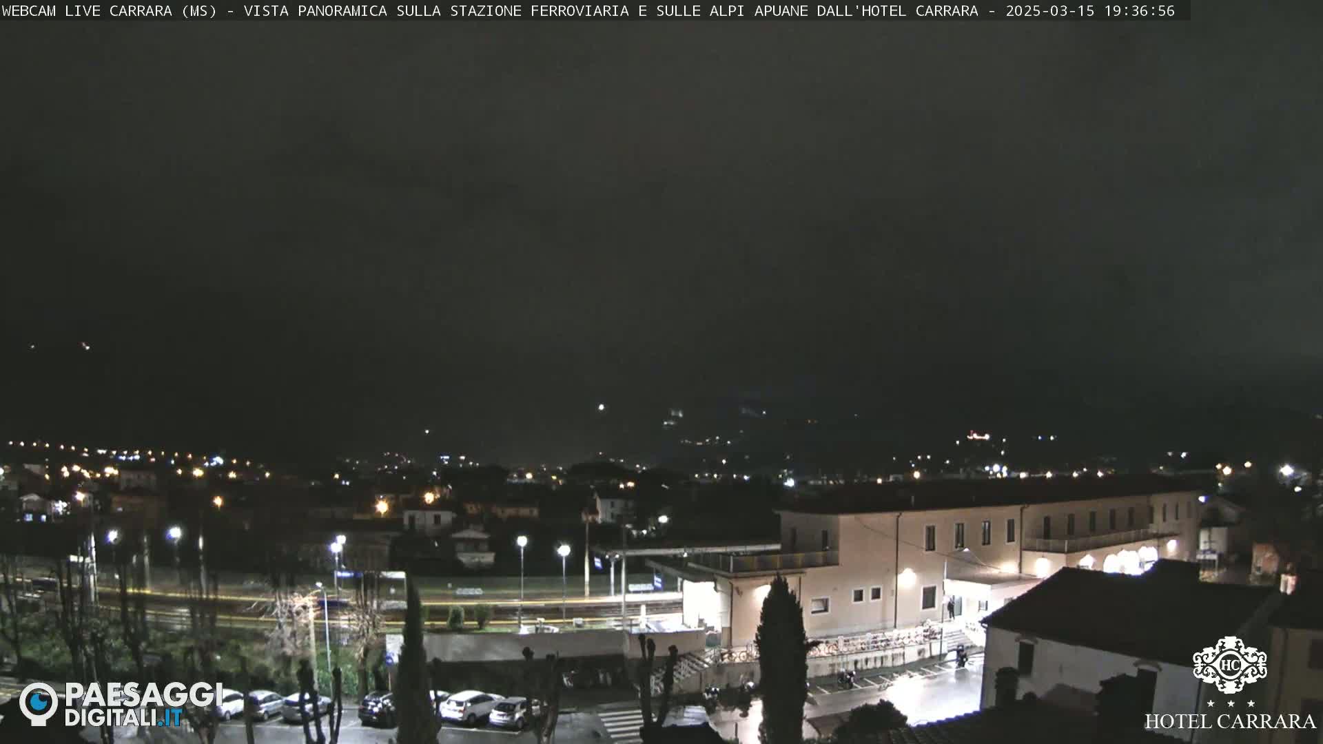 A nighttime view of a town with a train station and surrounding buildings under a dark, cloudy sky.
