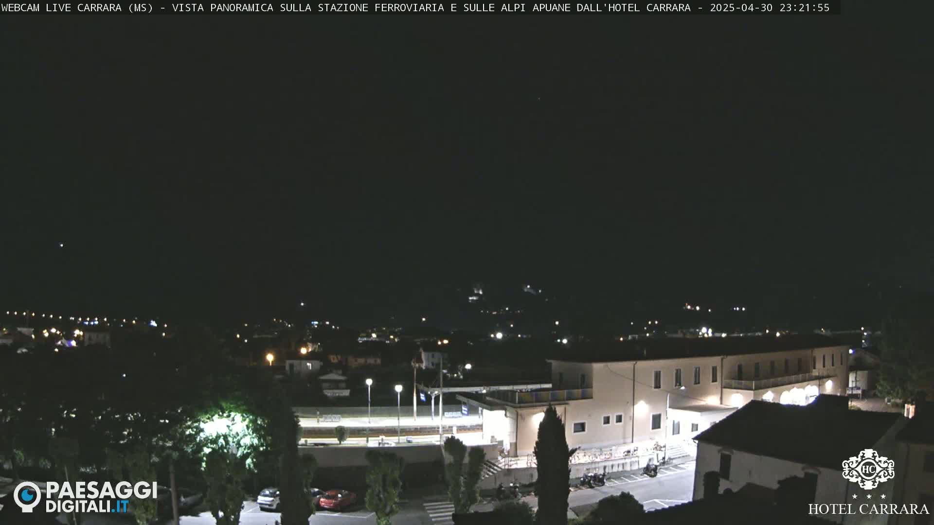 A nighttime panoramic view of a town, illuminated by streetlights, with a large building, possibly a hotel, in the foreground under a clear, dark sky.