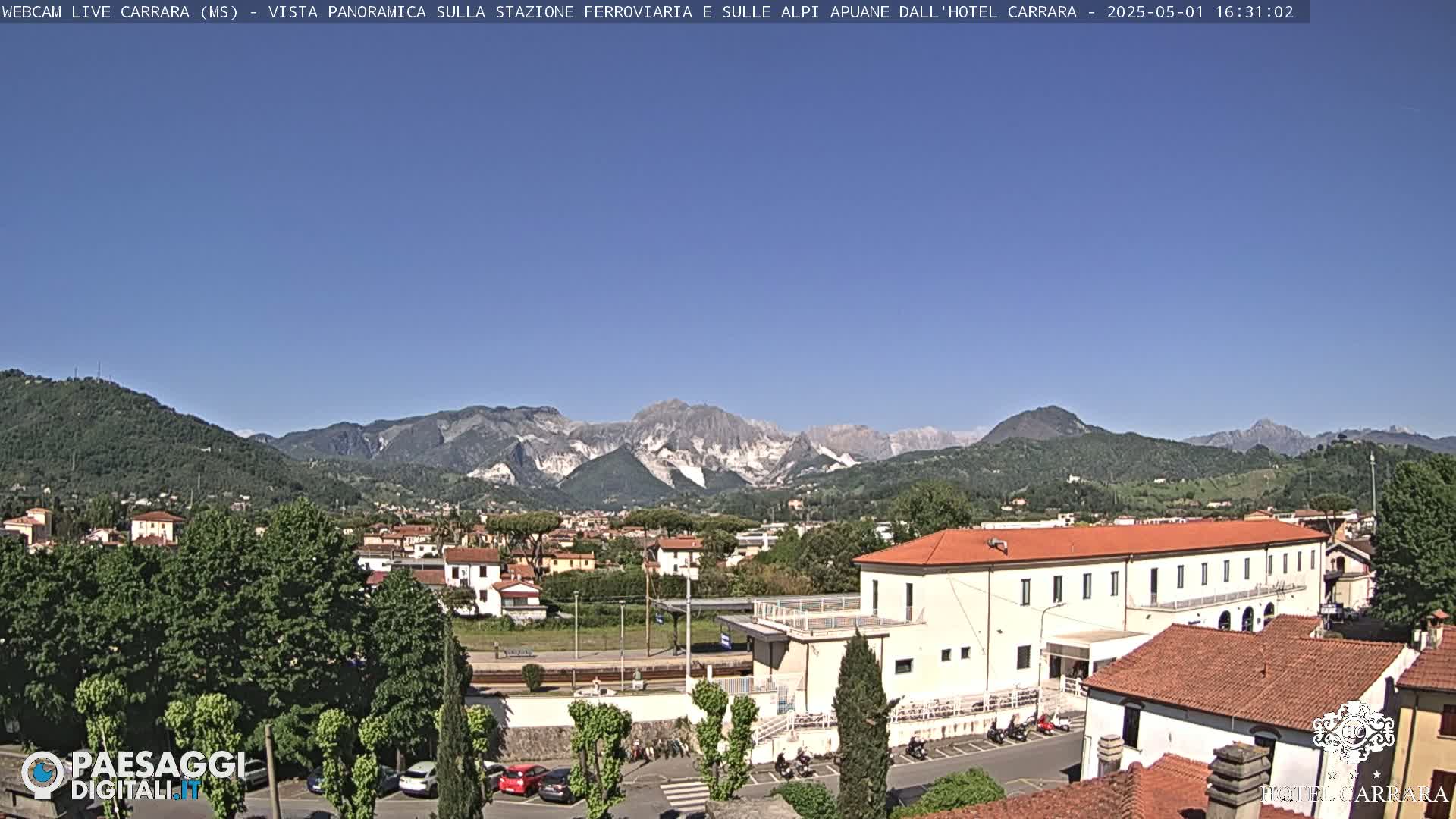A long, low building sits in a town at the base of a mountain range under a clear blue sky.