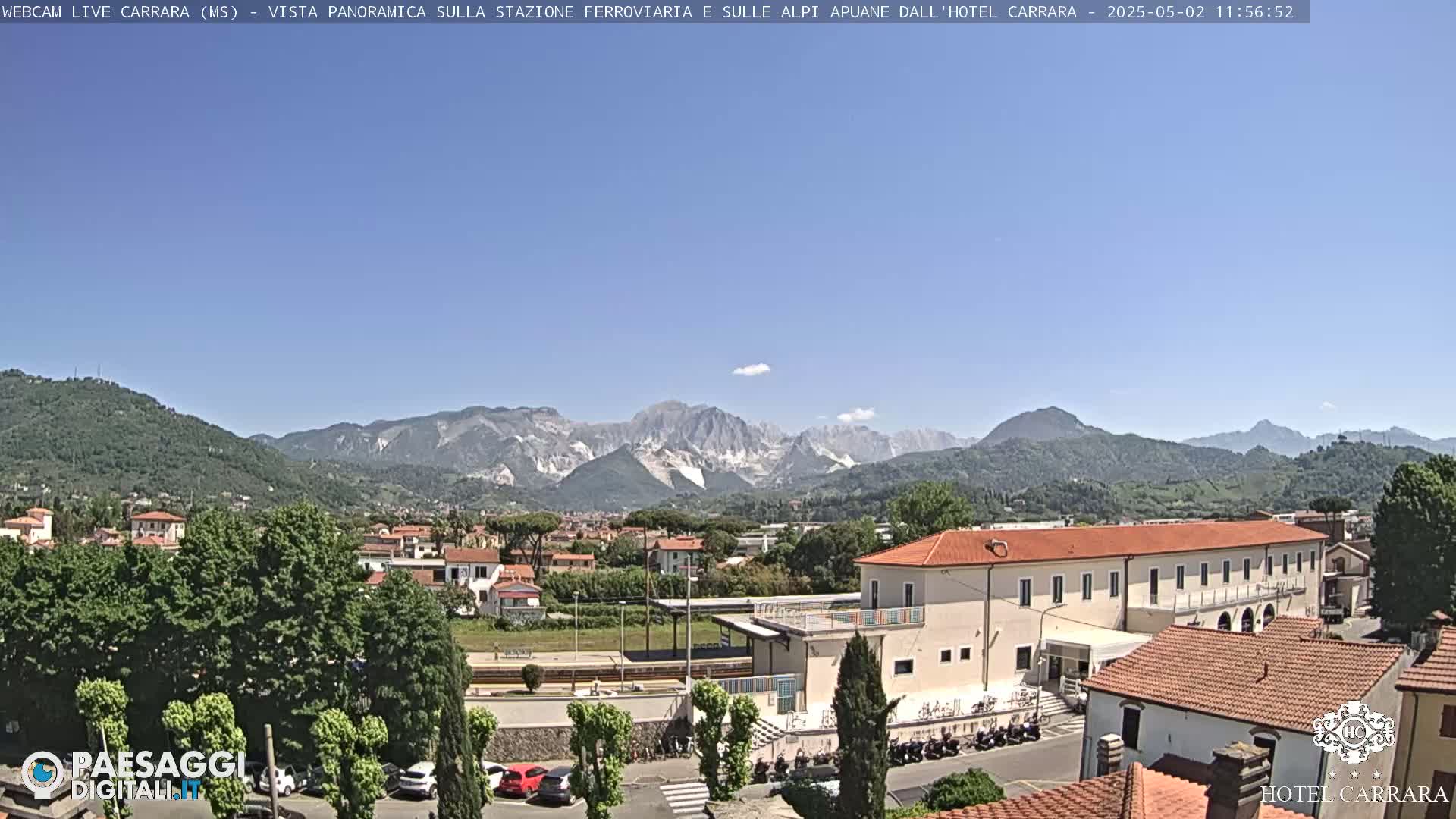 A panoramic view of a town nestled in a valley, with mountains in the background under a clear blue sky.