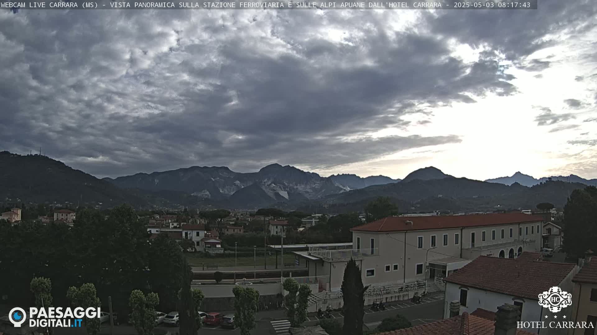 A cloudy sunrise illuminates a town nestled between mountains and a large hotel.