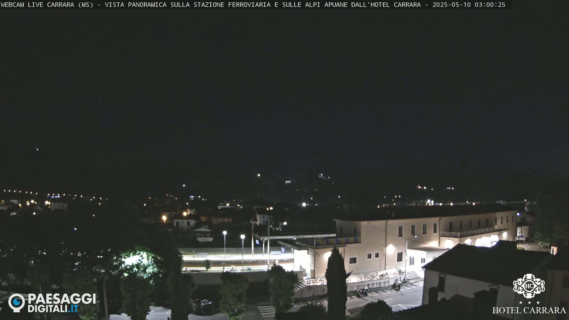 A nighttime, panoramic view of a town, featuring a large building and surrounding areas illuminated by artificial lights.