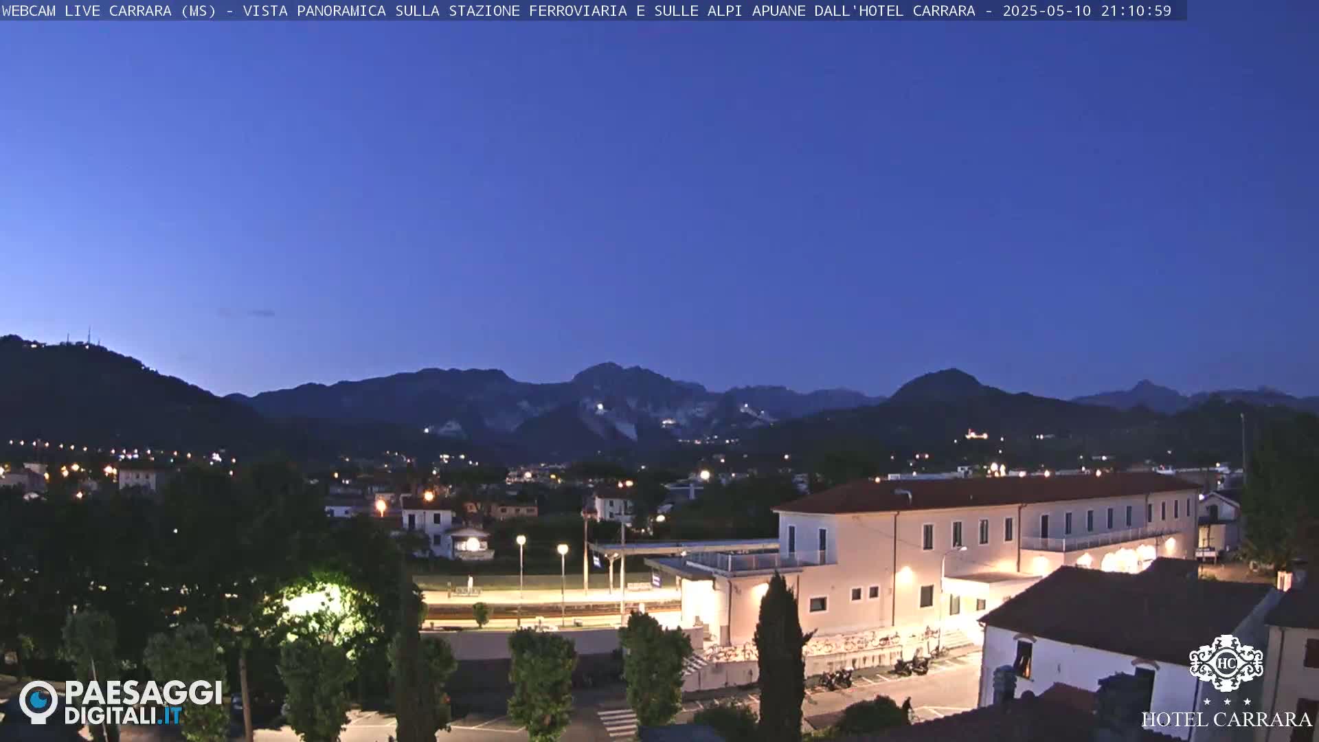 A nighttime view of a town nestled in a valley between mountains under a twilight sky.