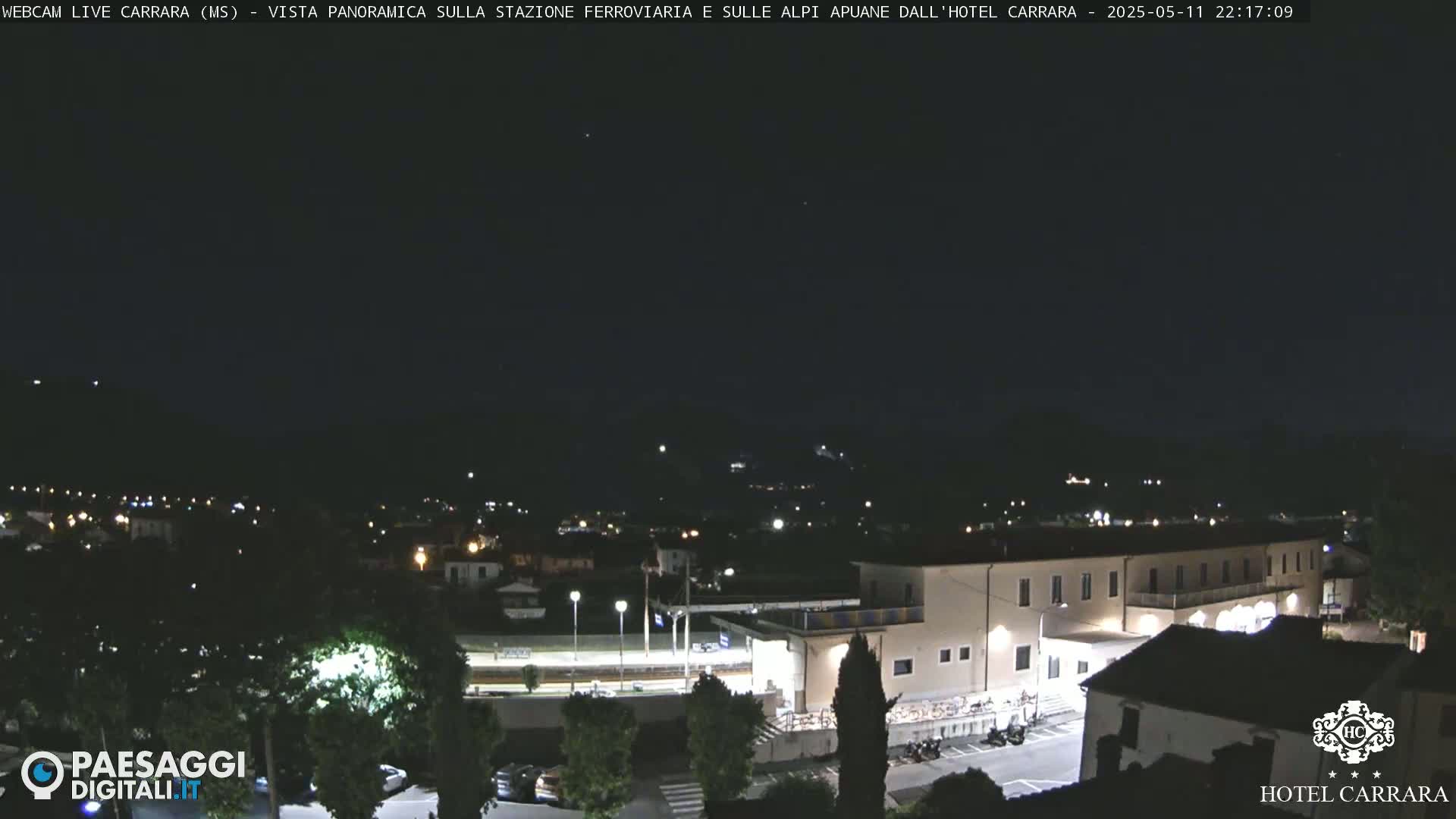 A nighttime, panoramic view of a town with a large building, possibly a hotel, illuminated, under a dark, clear sky.