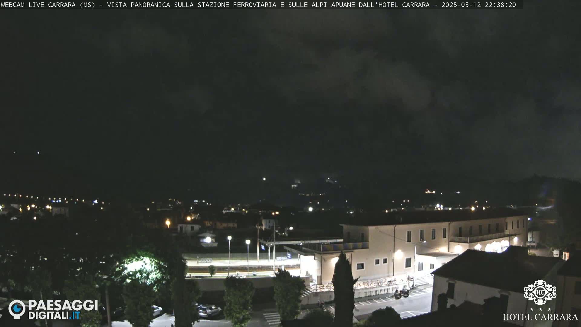 A nighttime view of a town with a train station and a large hotel, under a partly cloudy sky.