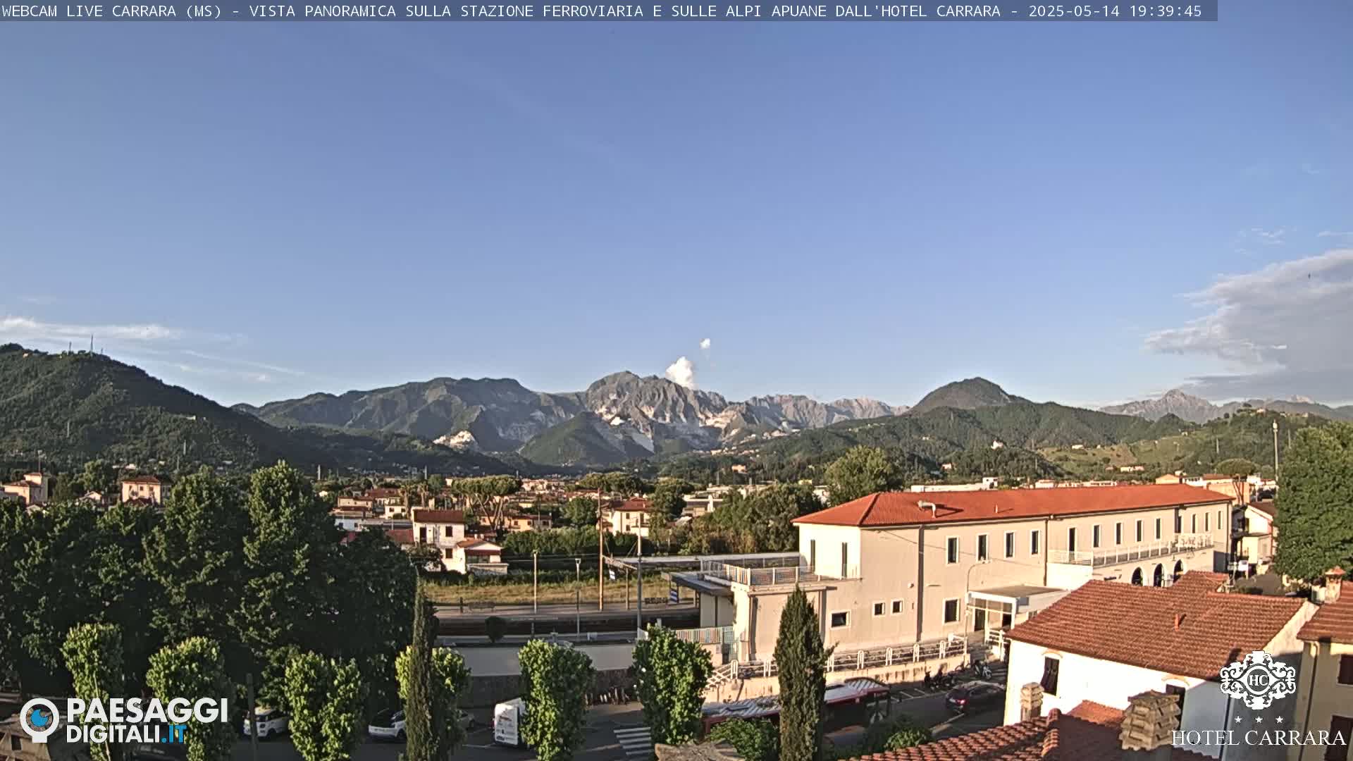 A long shot of a town nestled in a valley between mountains under a clear blue sky.