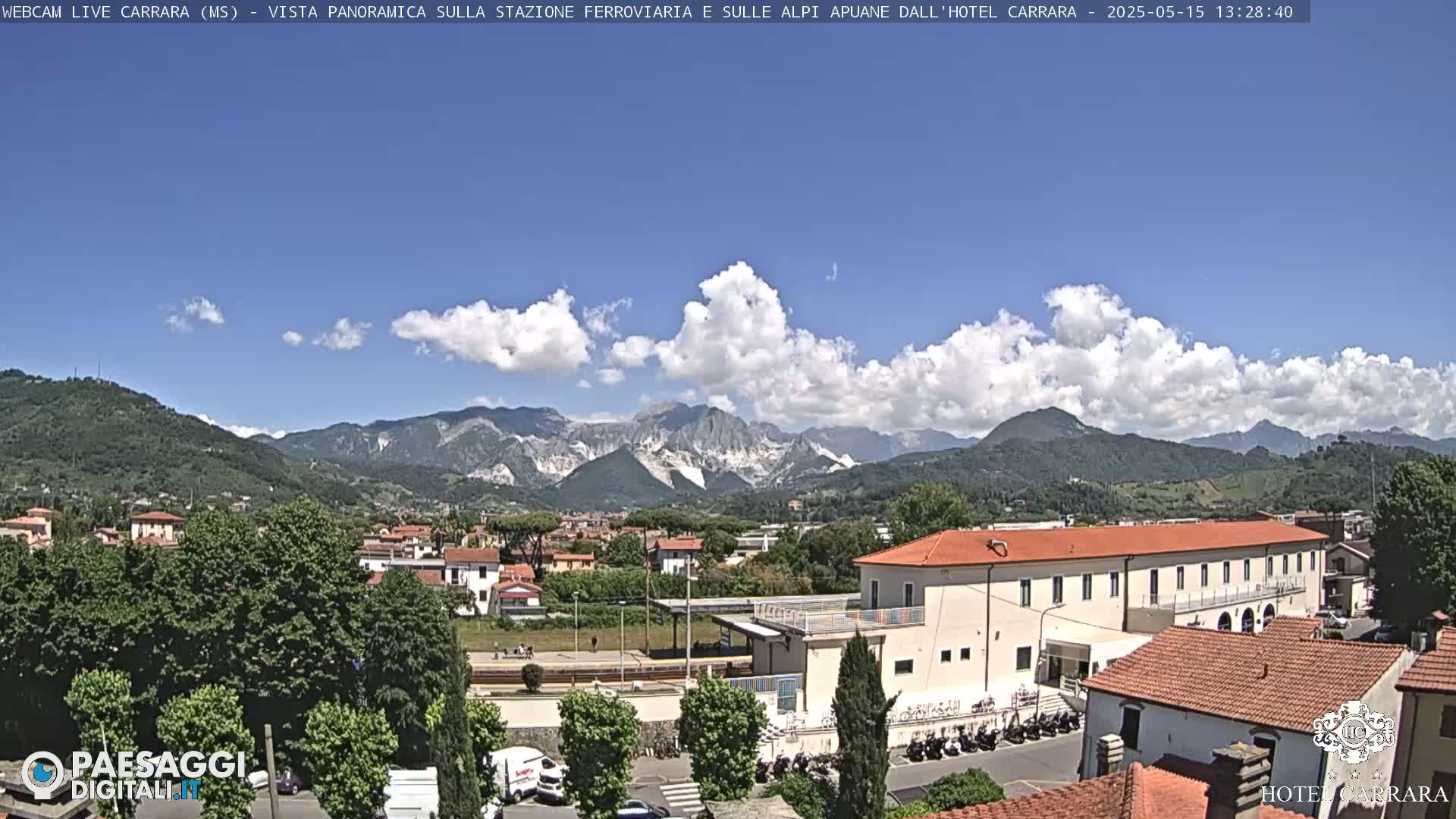 A partly cloudy day reveals a panoramic view of a town nestled in a valley, with mountains in the background.