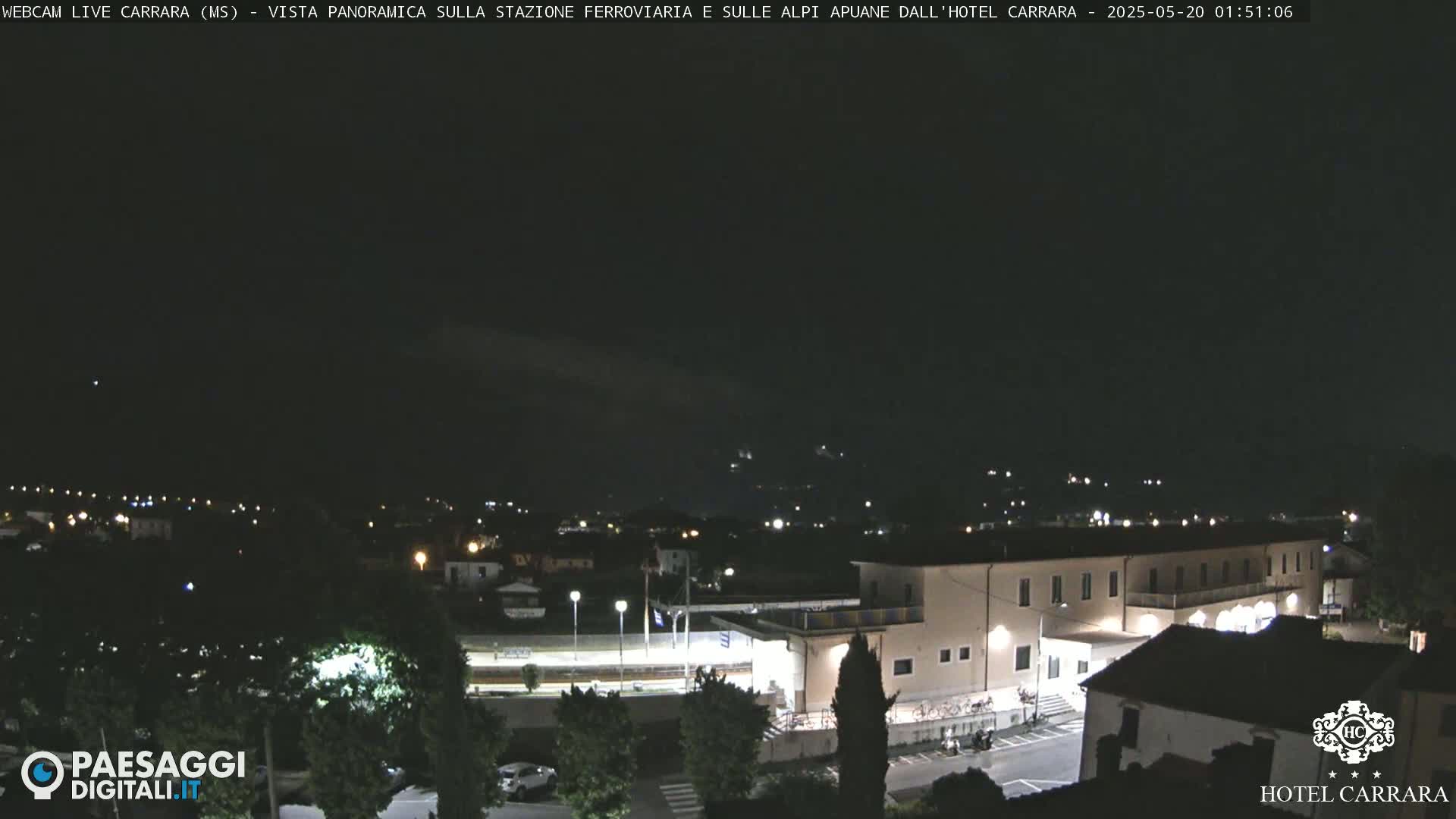 A nighttime panoramic view of a town with a large building, possibly a hotel, illuminated, under a dark, clear sky.