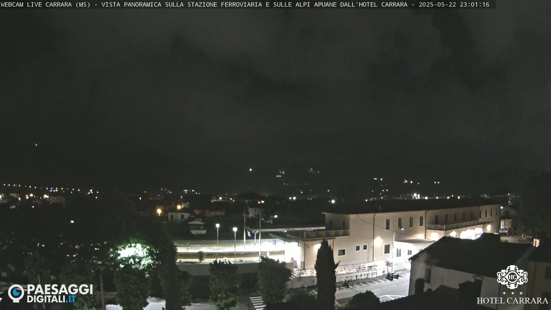 A nighttime, overcast view of a town with a large building, possibly a hotel, and a train station, illuminated by artificial lights.
