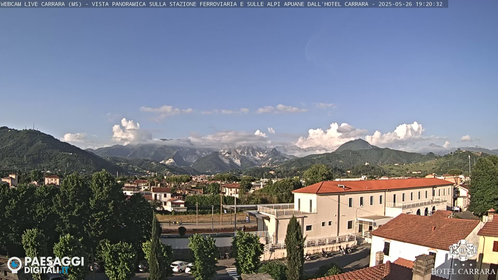 A partly cloudy day reveals a panoramic view of a town nestled in a valley, with mountains in the background.