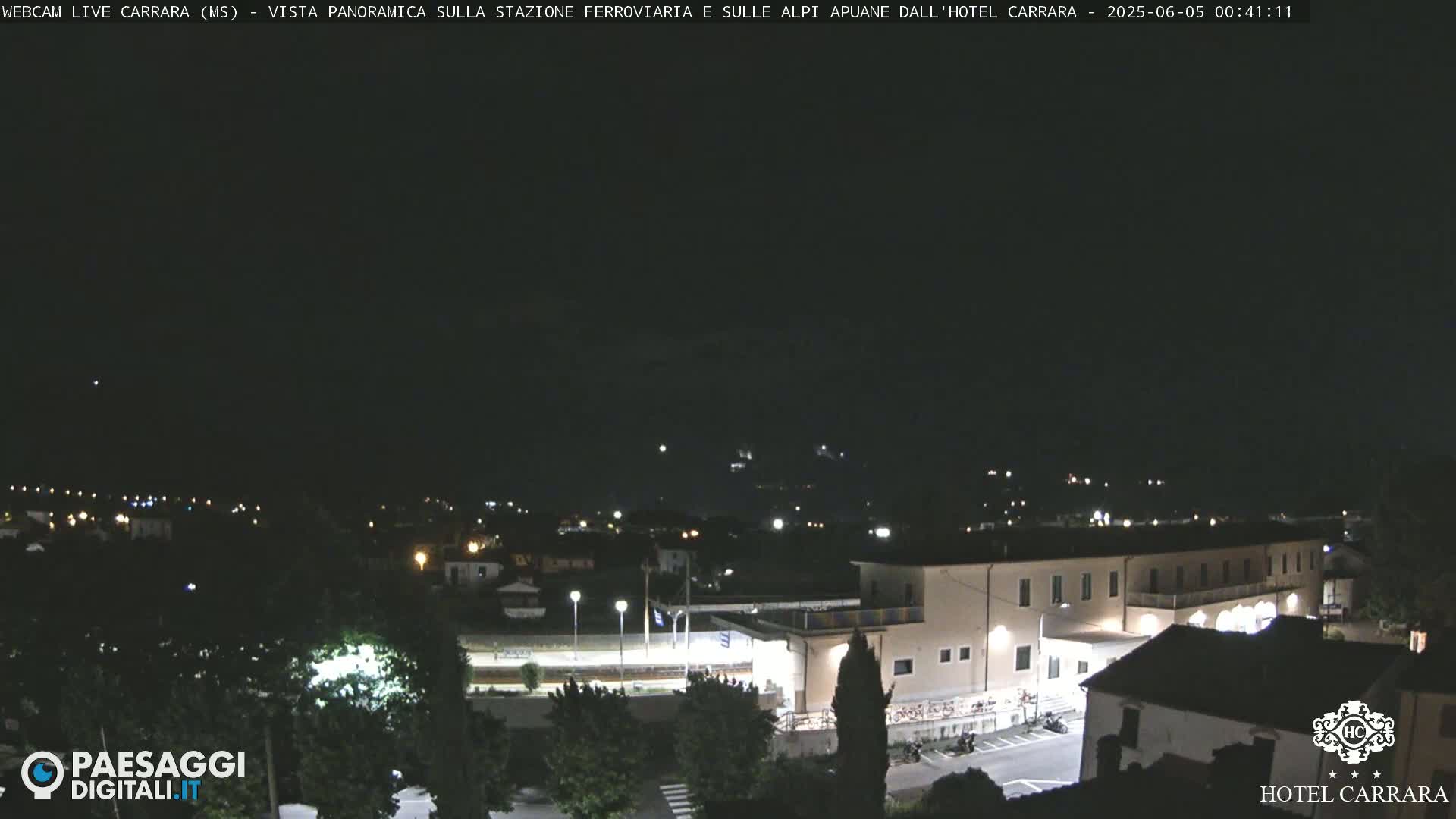 A nighttime, long shot of a town with a large building, possibly a hotel, illuminated, under a clear, dark sky.
