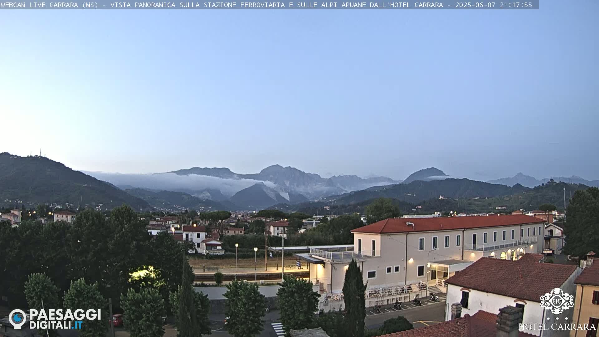A long shot of a town nestled in a valley, under a twilight sky, with mountains shrouded in fog in the background.