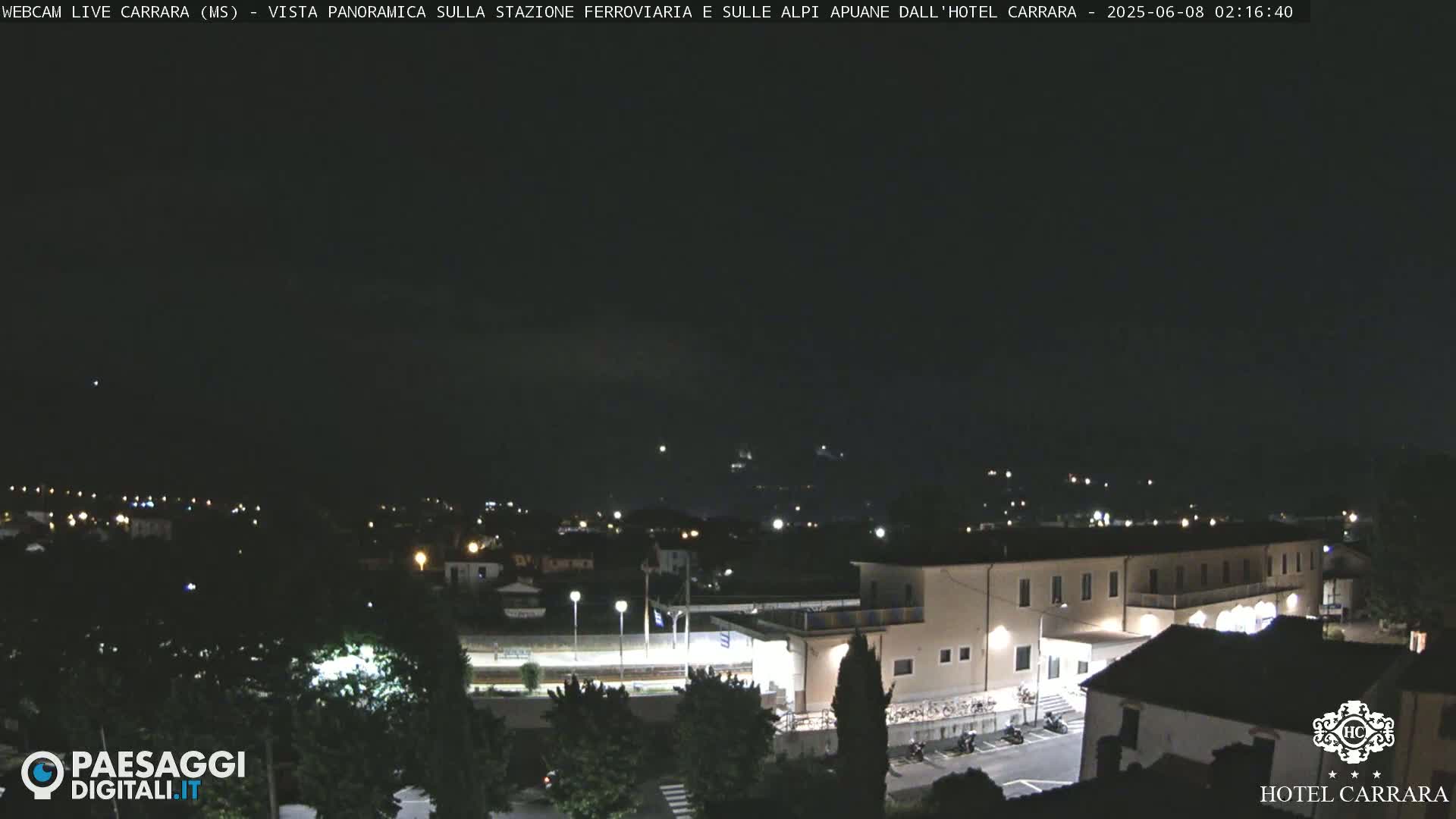 A nighttime, panoramic view of a town, featuring a large building and train station, under a clear, dark sky.