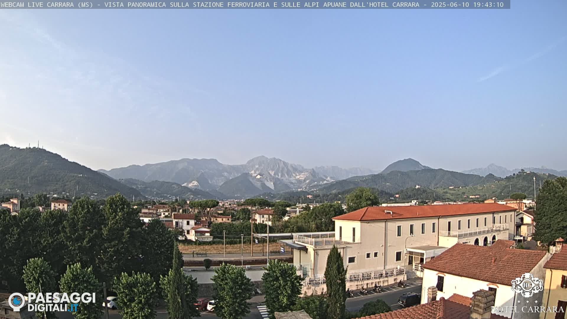 A panoramic view of a town nestled in a valley, with mountains in the background under a clear, light-blue sky.